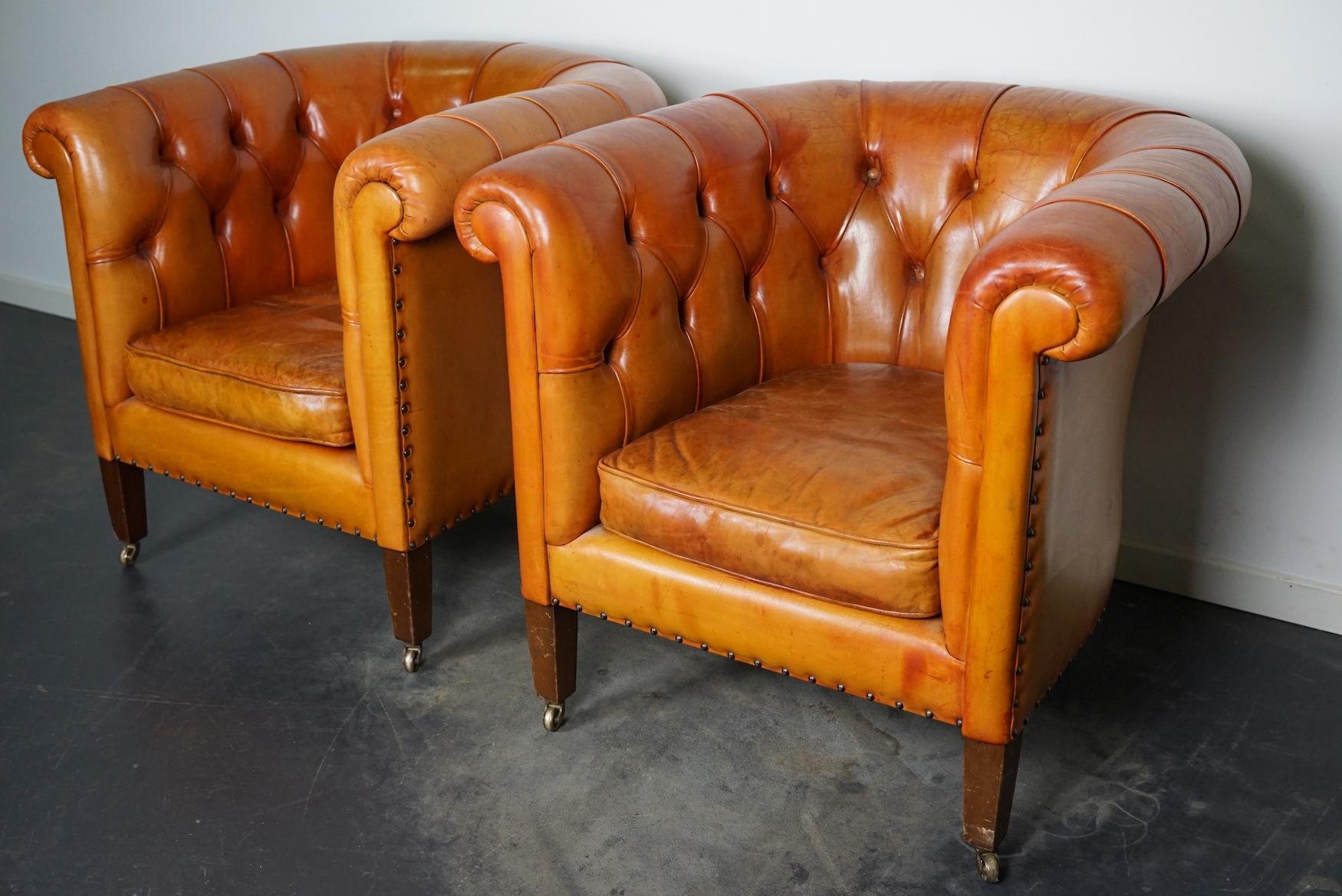 This pair of cognac-colored leather club chairs come from the Netherlands. They are upholstered with cognac-colored leather and feature metal rivets and wooden legs. The buttoned backs give this pair an exclusive look.