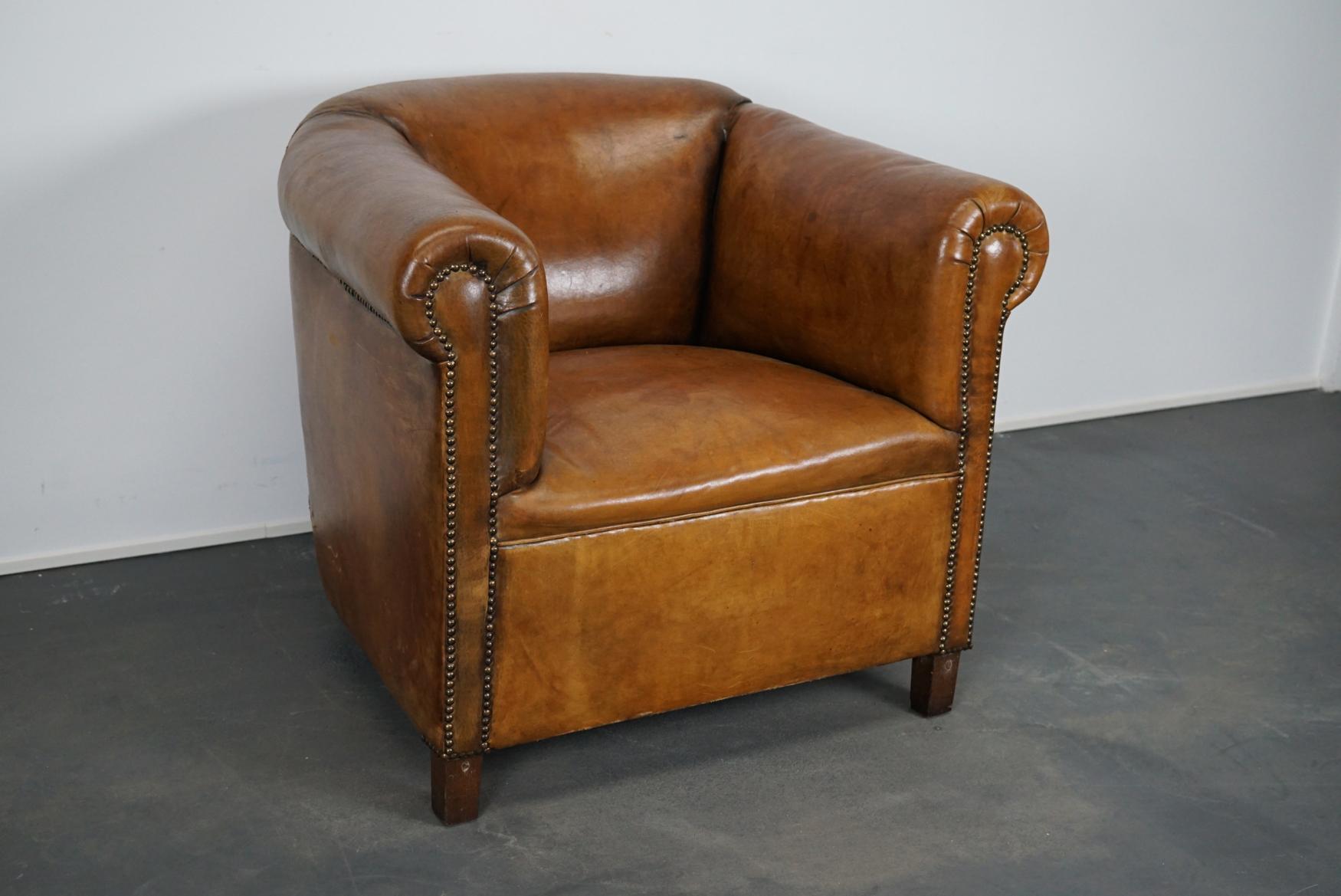 This cognac-colored leather club chair comes from the Netherlands. It is upholstered with cognac-colored leather and features metal rivets and wooden legs.