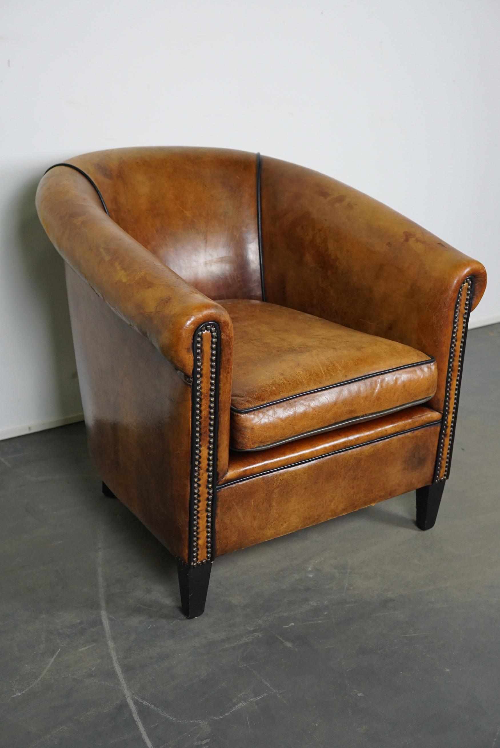 This cognac-colored leather club chair comes from the Netherlands. It is upholstered with cognac-colored leather and features metal rivets and wooden legs.