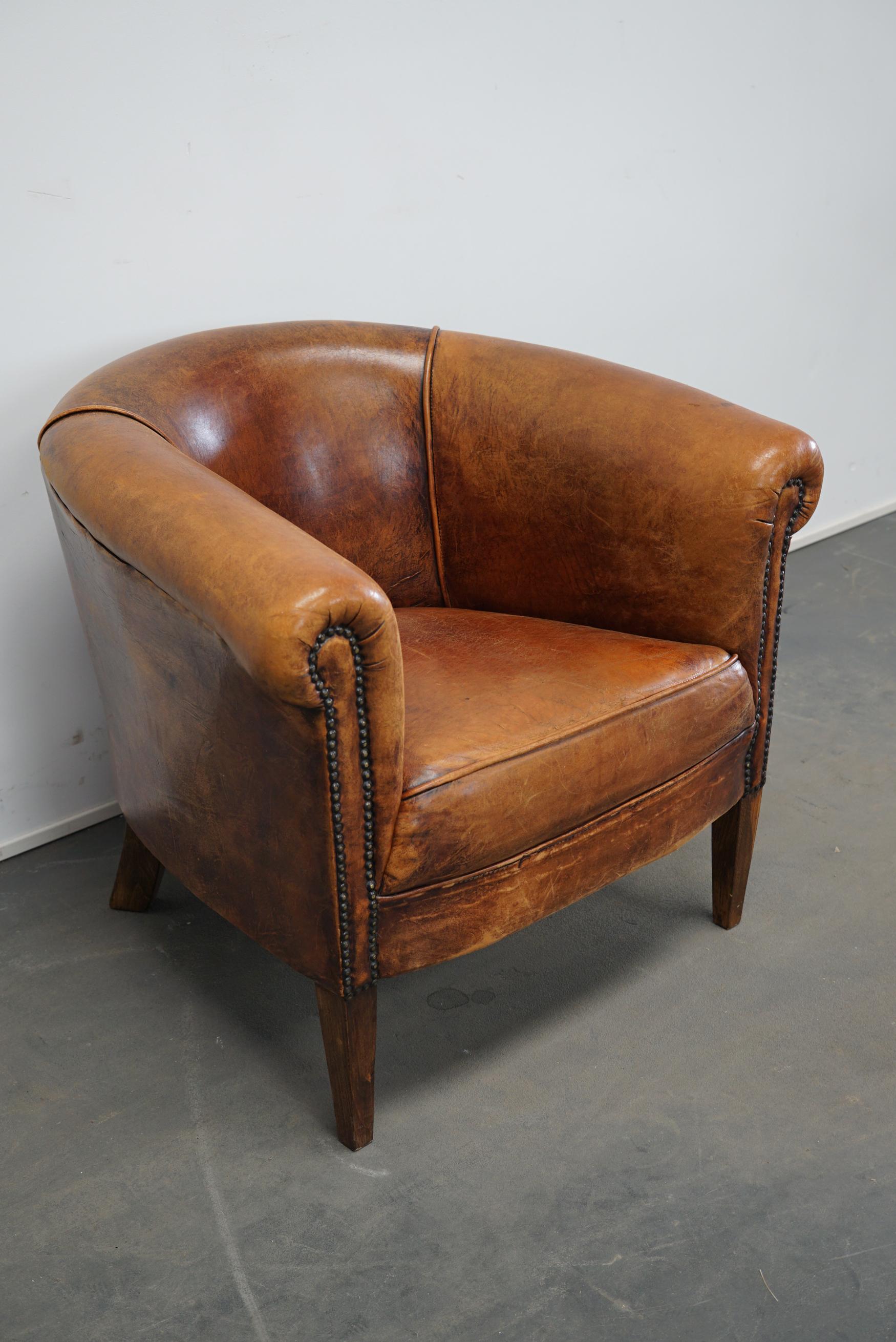 This cognac-colored leather club chair comes from the Netherlands. It is upholstered with cognac-colored leather and features metal rivets and wooden legs.