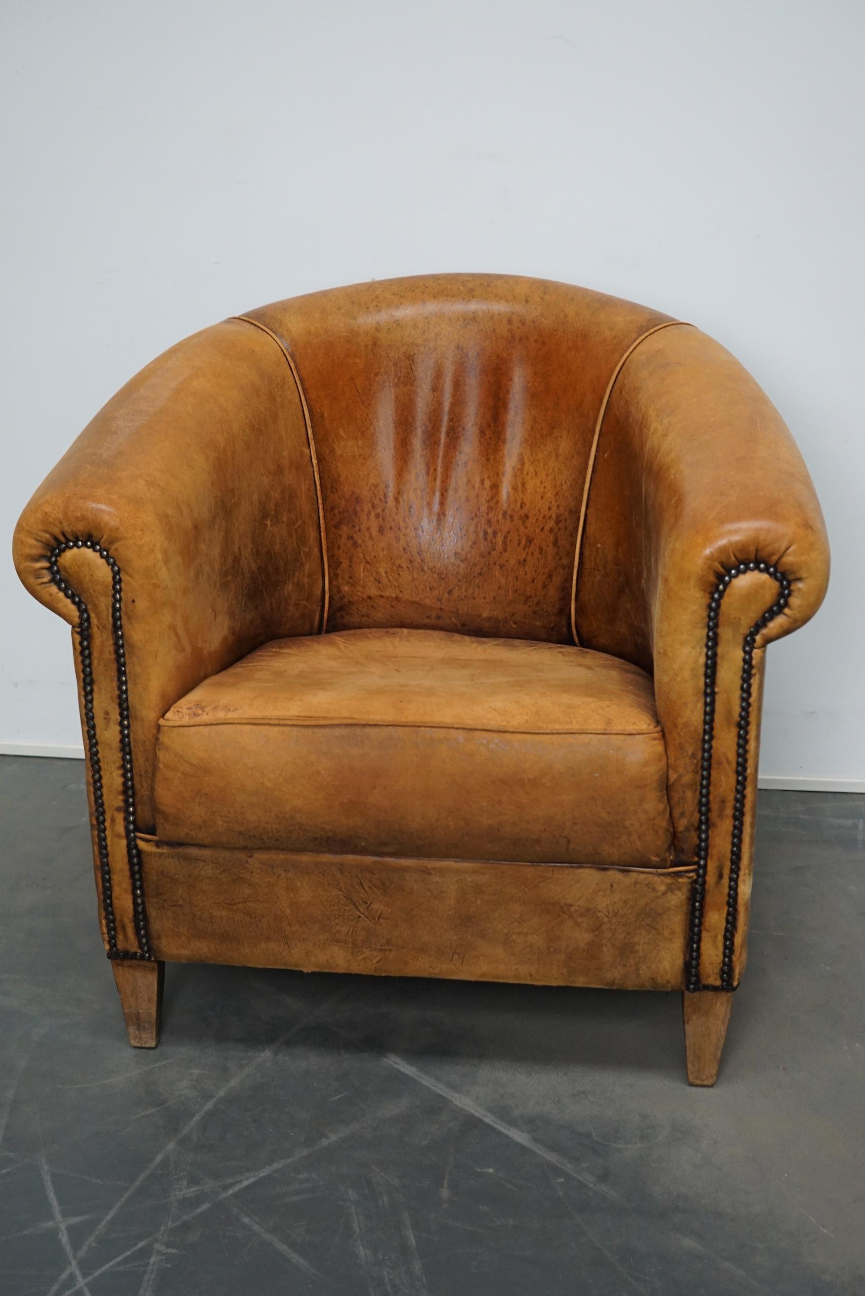 This vintage club chair is upholstered with cognac-colored leather and features metal rivets and wooden legs.