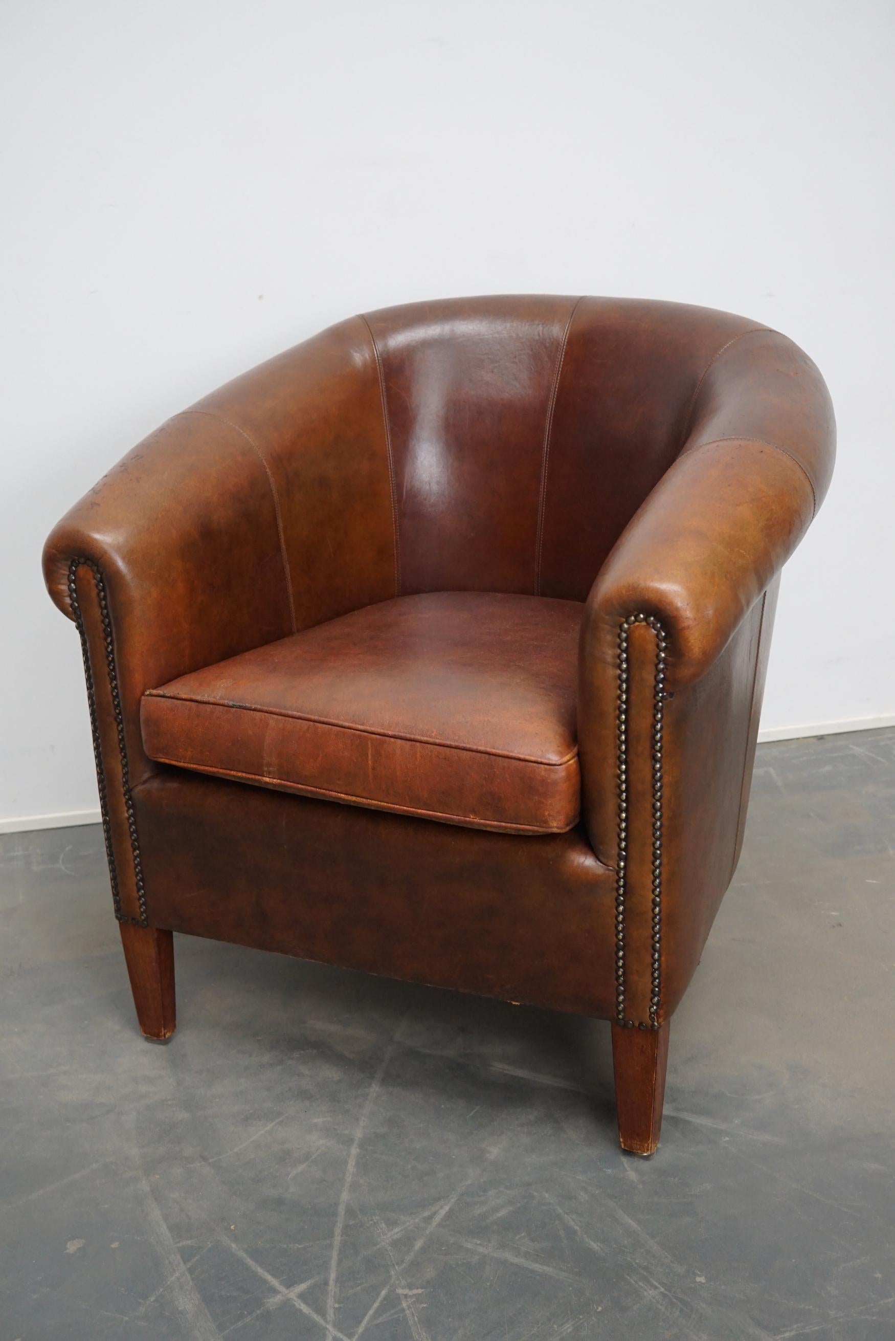 This vintage club chair is upholstered with cognac-colored leather and features metal rivets and wooden legs.
 
 