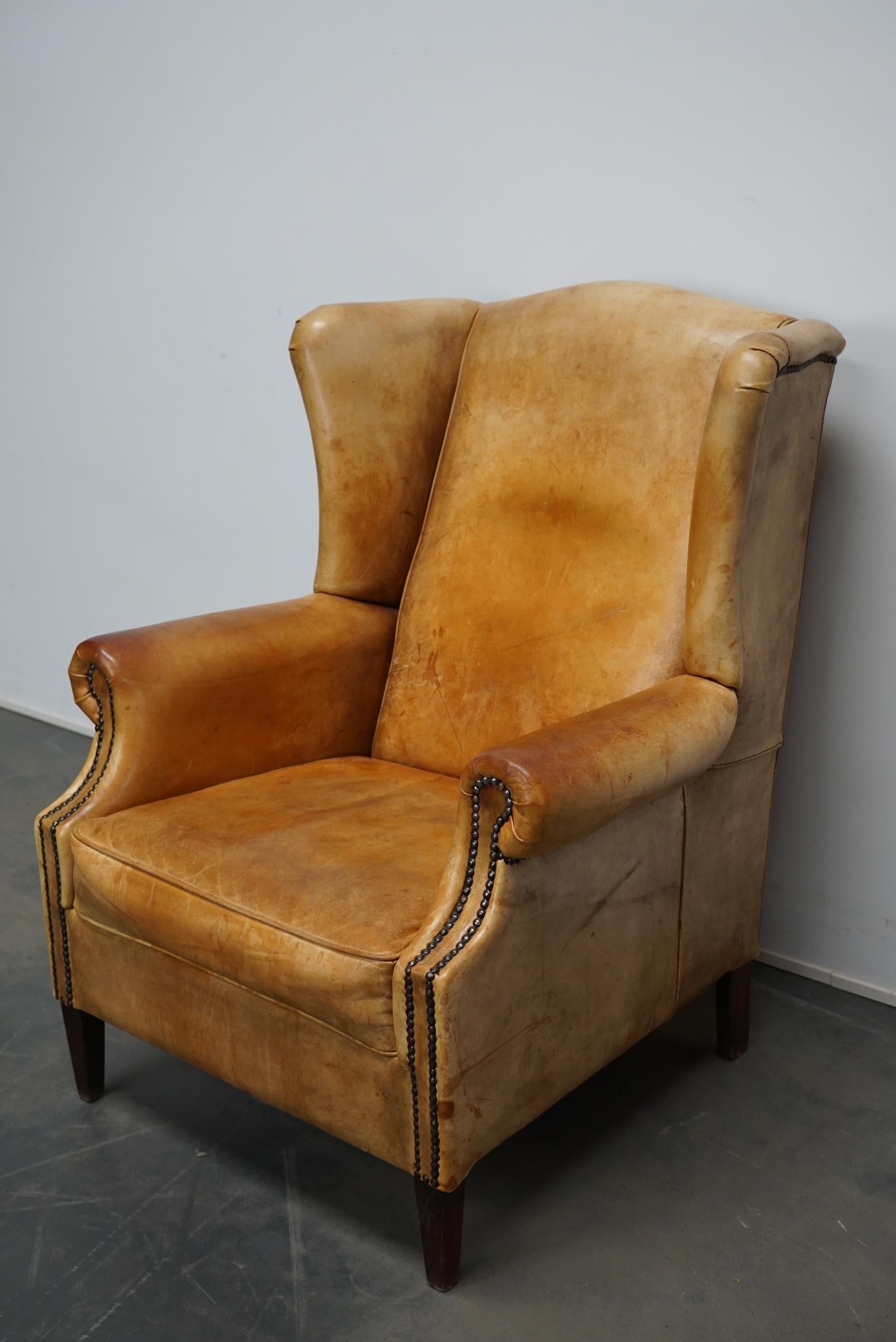 This vintage club chair is upholstered with cognac-colored leather and features metal rivets and wooden legs.