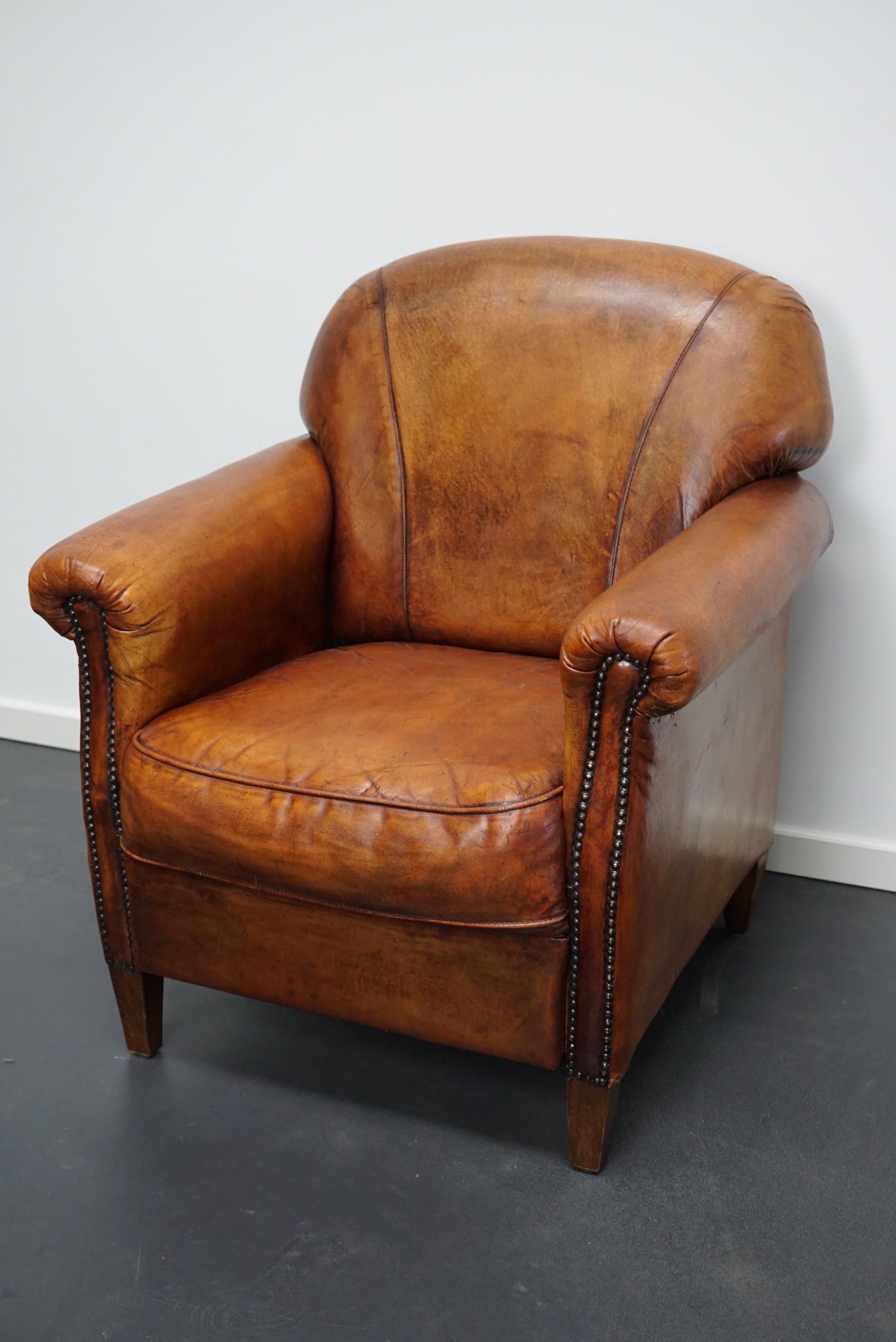 This vintage club chair is upholstered with cognac-colored leather and features metal rivets and wooden legs.
Details.
  