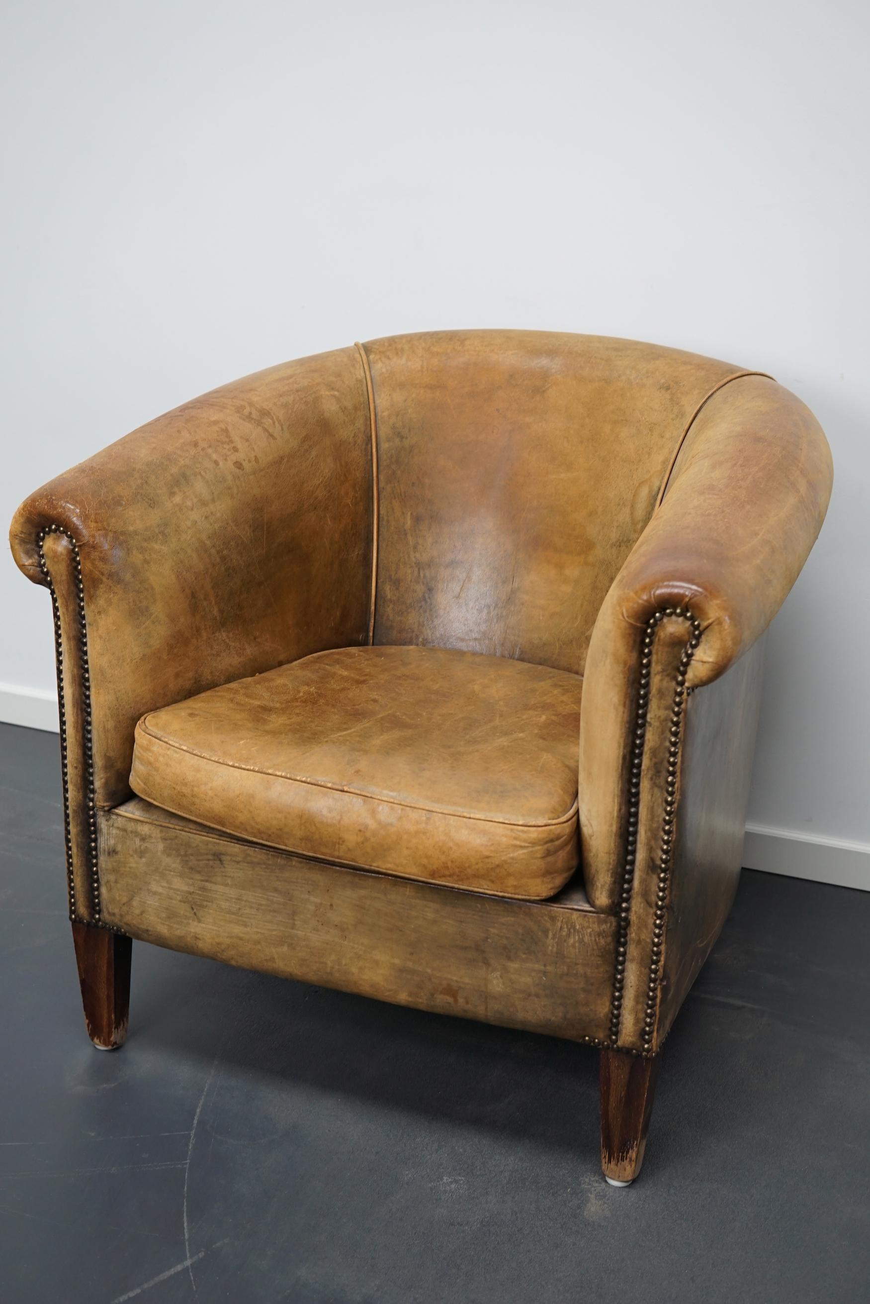 This vintage club chair is upholstered with cognac-colored leather and features metal rivets and wooden legs.