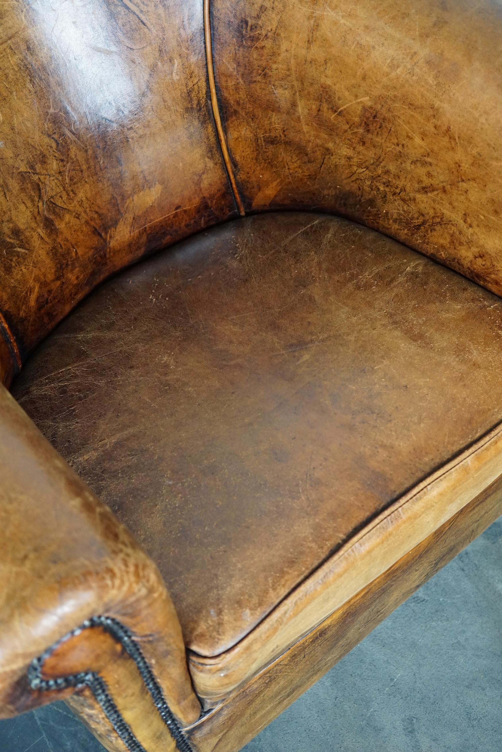 This vintage club chair is upholstered with cognac-colored leather and features metal rivets and wooden legs.
 