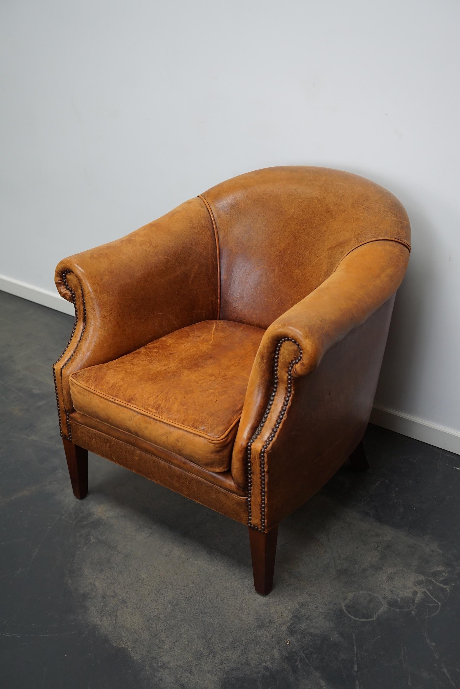 This cognac-colored leather club chair comes from the Netherlands. It is upholstered with cognac-colored leather and features metal rivets and wooden legs.