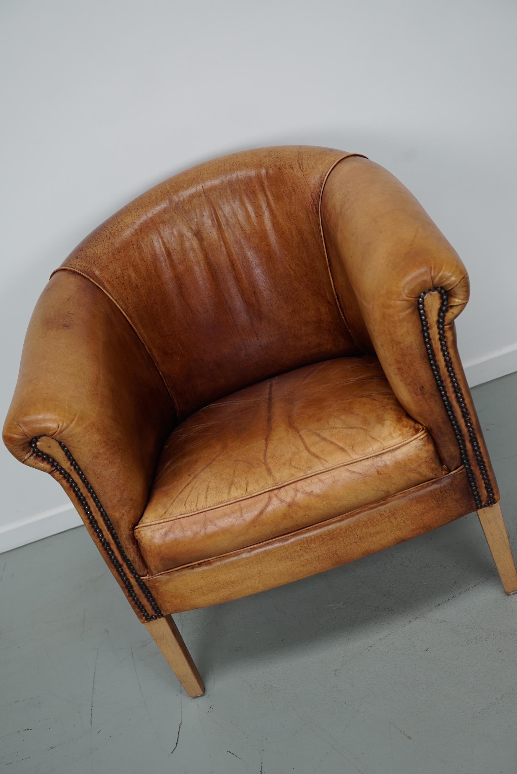 Ce fauteuil club en cuir de couleur cognac provient des Pays-Bas. Il est recouvert de cuir de couleur cognac et comporte des rivets en métal et des pieds en bois.