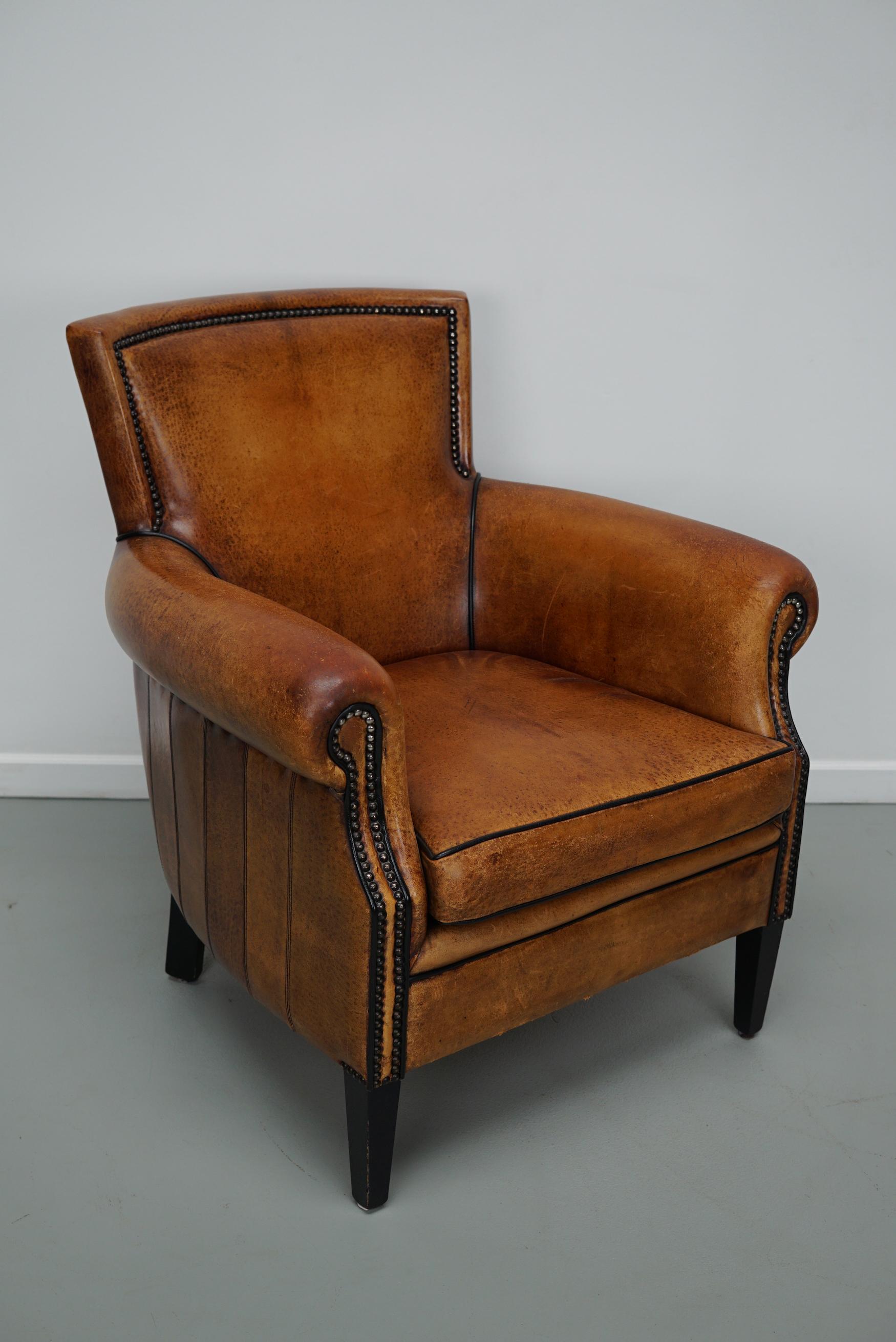 This cognac-colored leather club chair comes from the Netherlands. It is upholstered with cognac-colored leather and features metal rivets and wooden legs.
