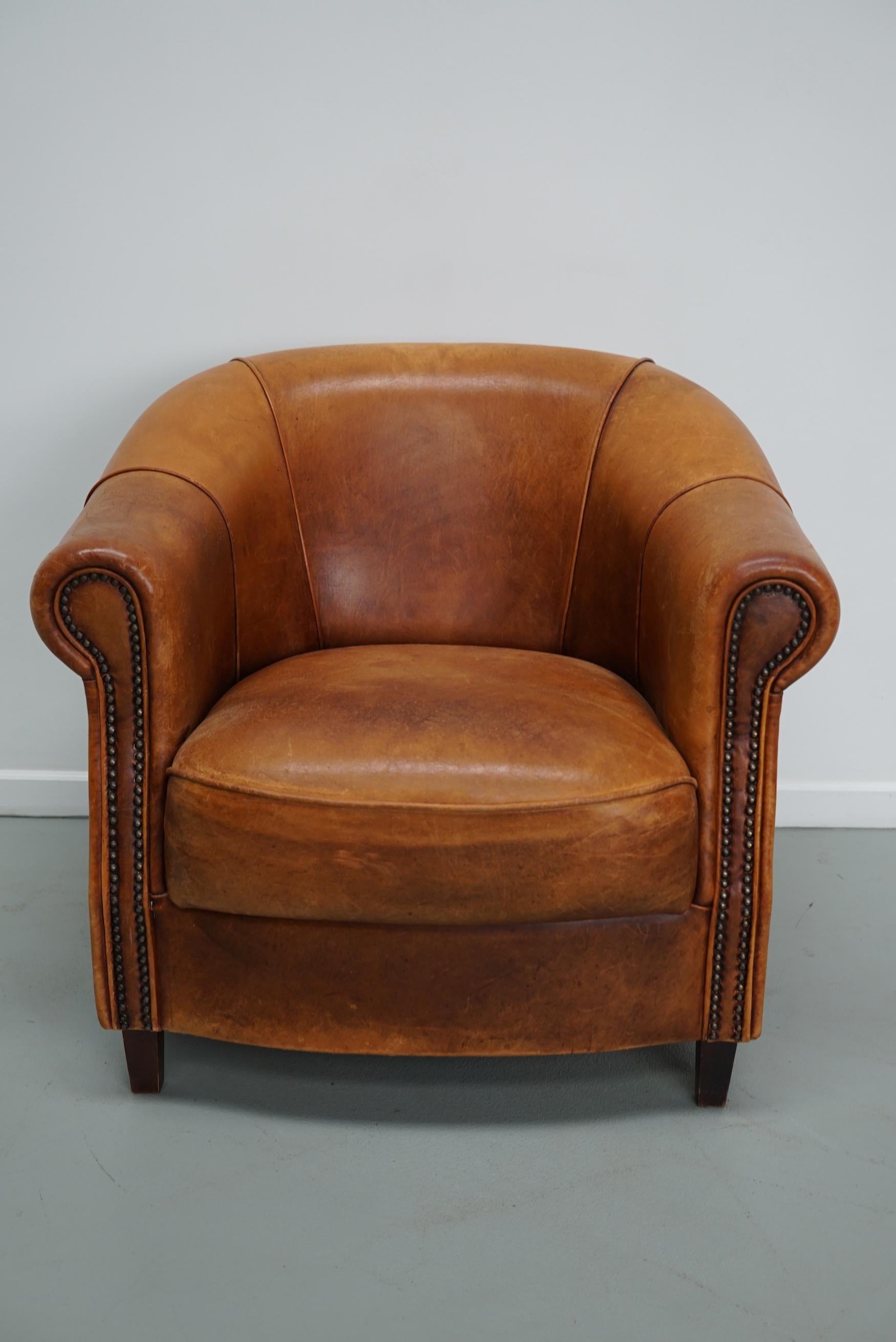 This cognac-colored leather club chair comes from the Netherlands. It is upholstered with cognac-colored leather and features metal rivets and wooden legs.