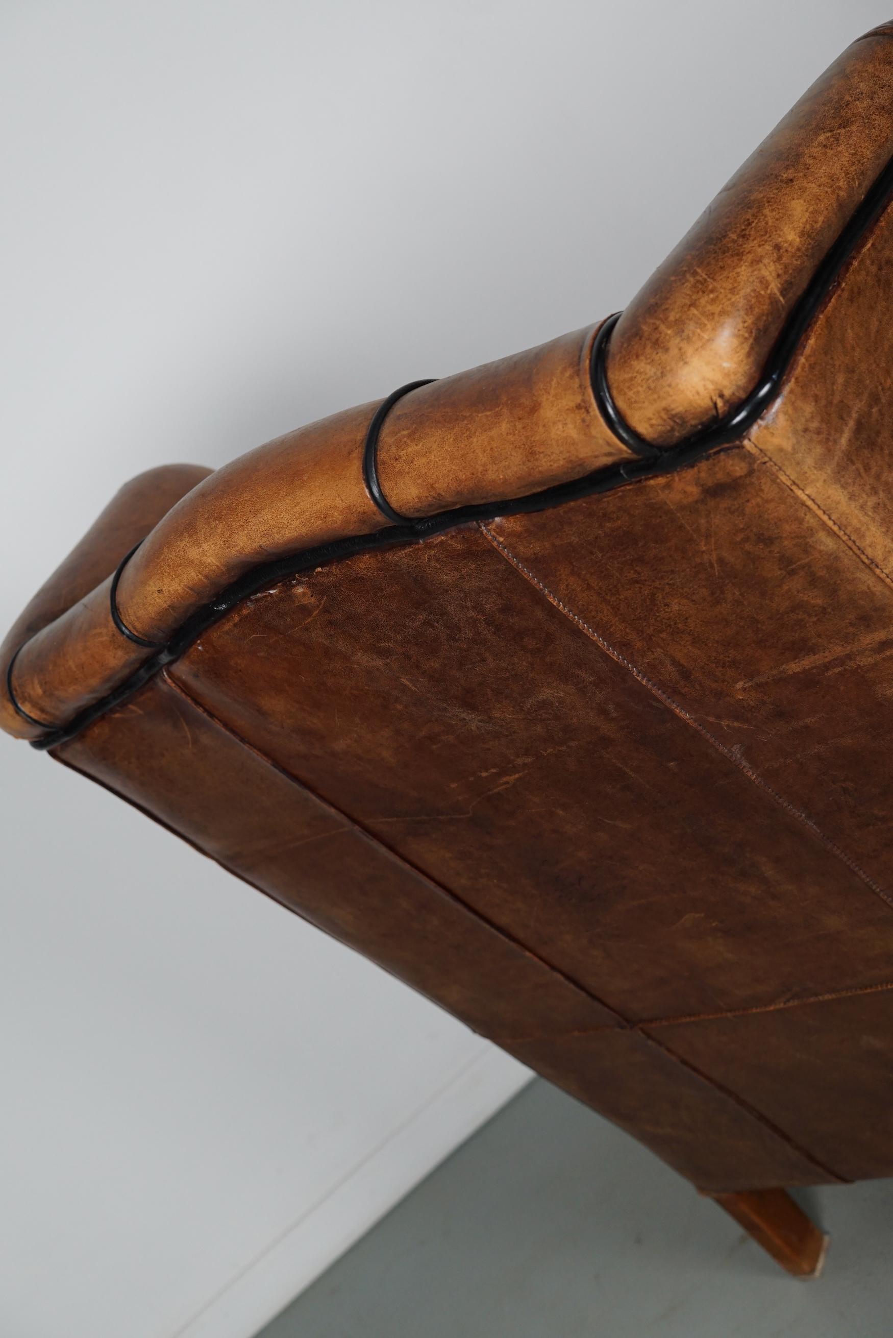 This cognac-colored leather club chair comes from the Netherlands. It is upholstered with cognac-colored leather and features metal rivets and wooden legs.