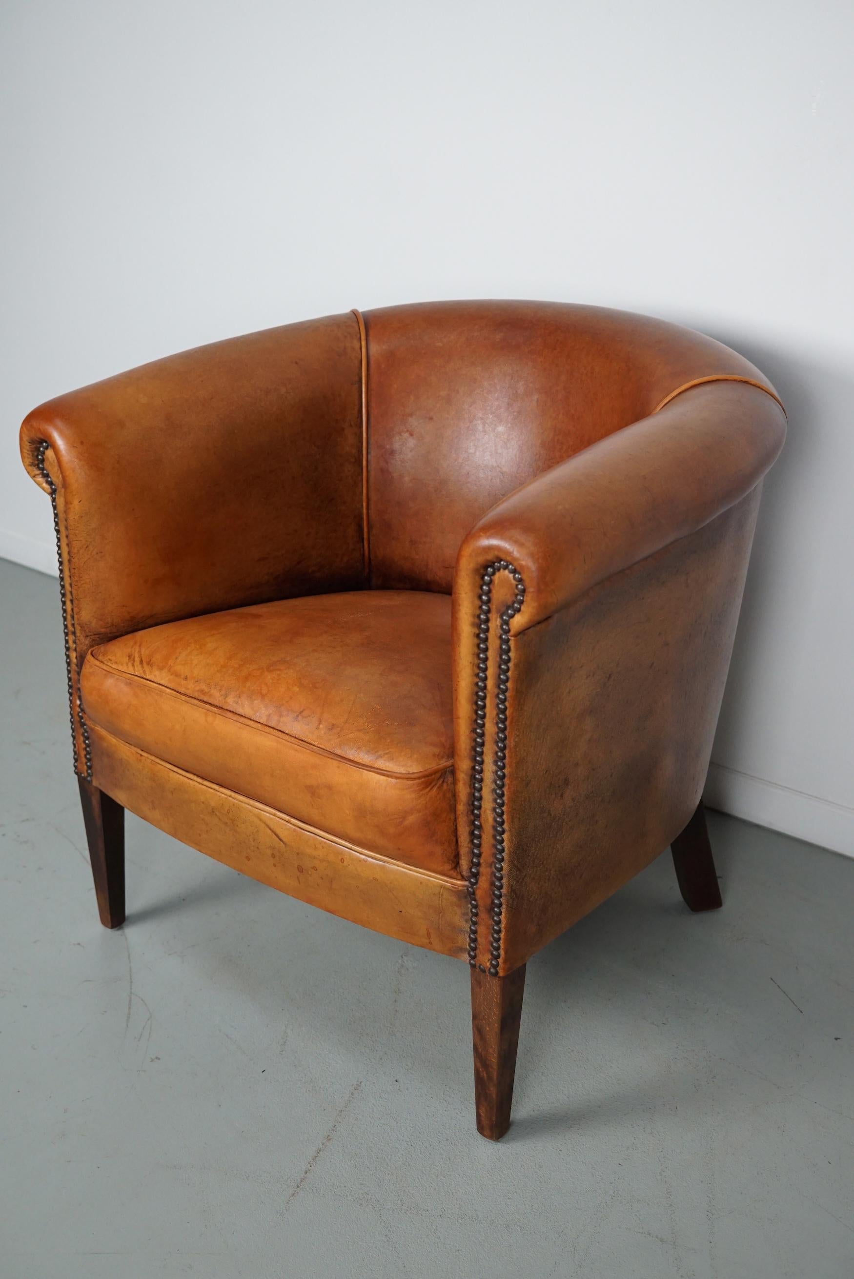 This cognac-colored leather club chair comes from the Netherlands. It is upholstered with cognac-colored leather and features metal rivets and wooden legs.