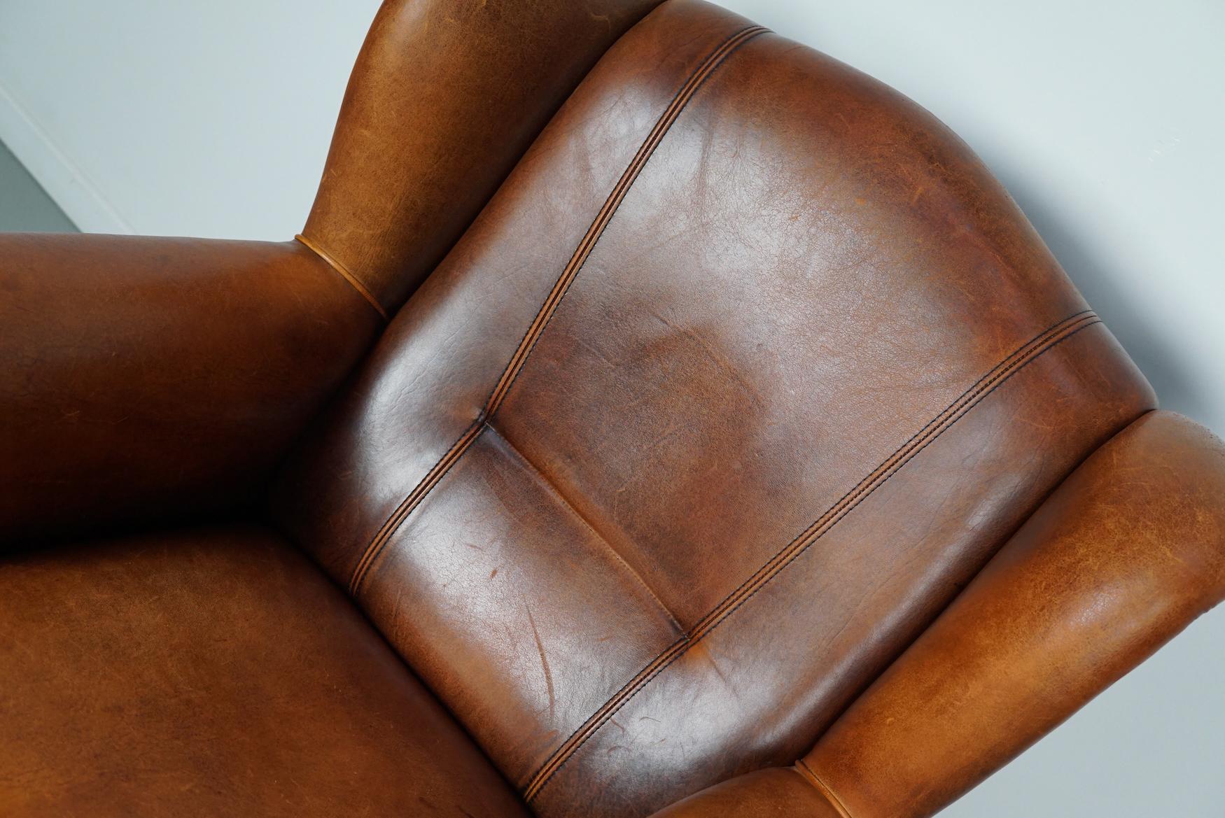 This cognac-colored leather club chair comes from the Netherlands. It is upholstered with cognac-colored leather and features metal rivets and wooden legs.