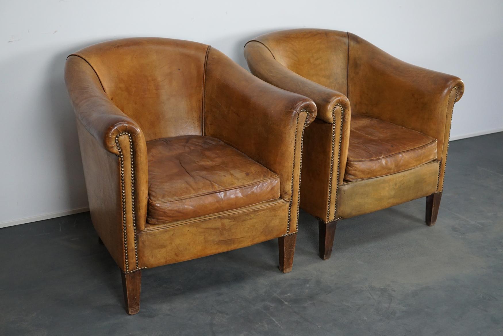 This pair of cognac-colored leather club chairs come from the Netherlands. They are upholstered with cognac-colored leather and feature metal rivets and wooden legs.
      