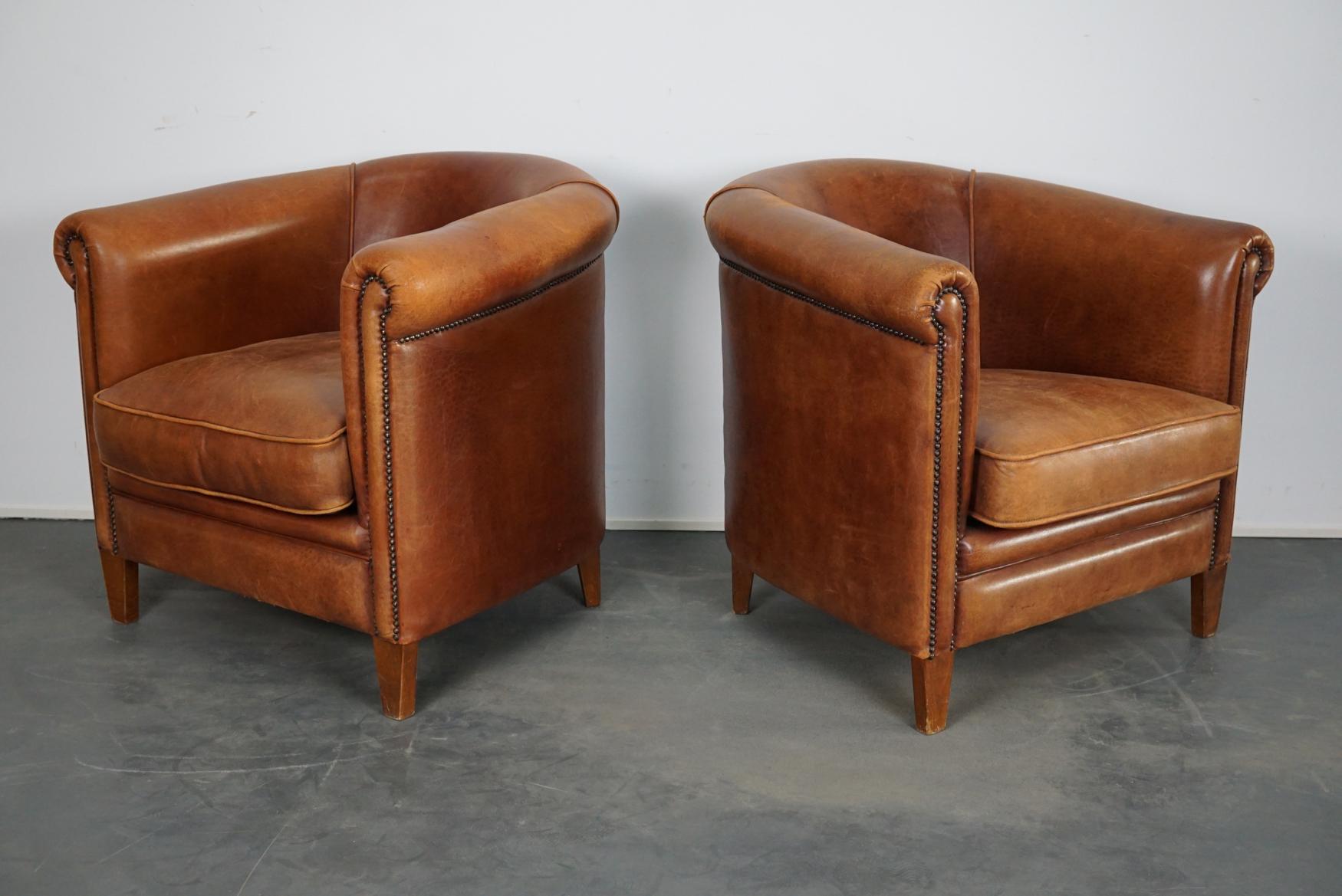 This pair of cognac-colored leather club chairs come from the Netherlands. They are upholstered with cognac-colored leather and feature metal rivets and wooden legs.
           