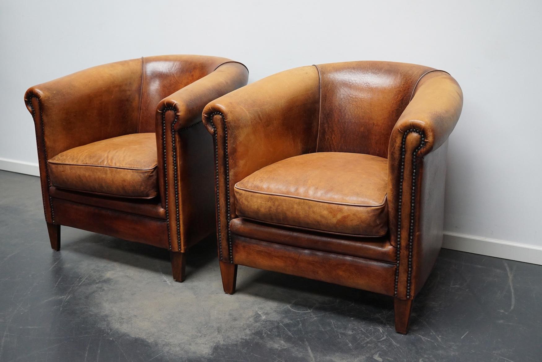 Cette paire de fauteuils club en cuir de couleur cognac provient des Pays-Bas. Ils sont recouverts de cuir de couleur cognac et présentent des rivets en métal et des pieds en bois.