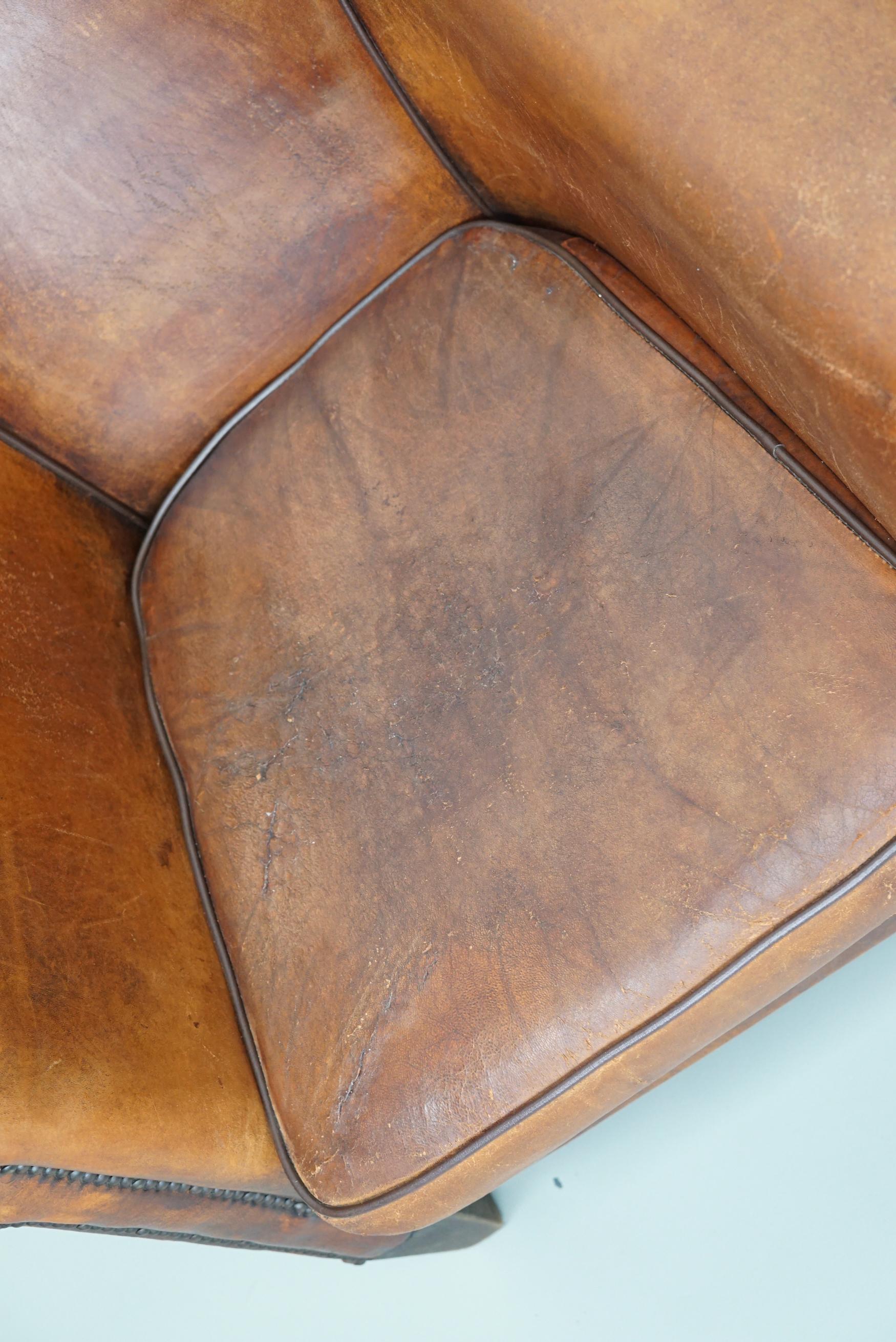 Cette paire de fauteuils club en cuir de couleur cognac provient des Pays-Bas. Ils sont recouverts de cuir de couleur cognac et présentent des rivets en métal et des pieds en bois.