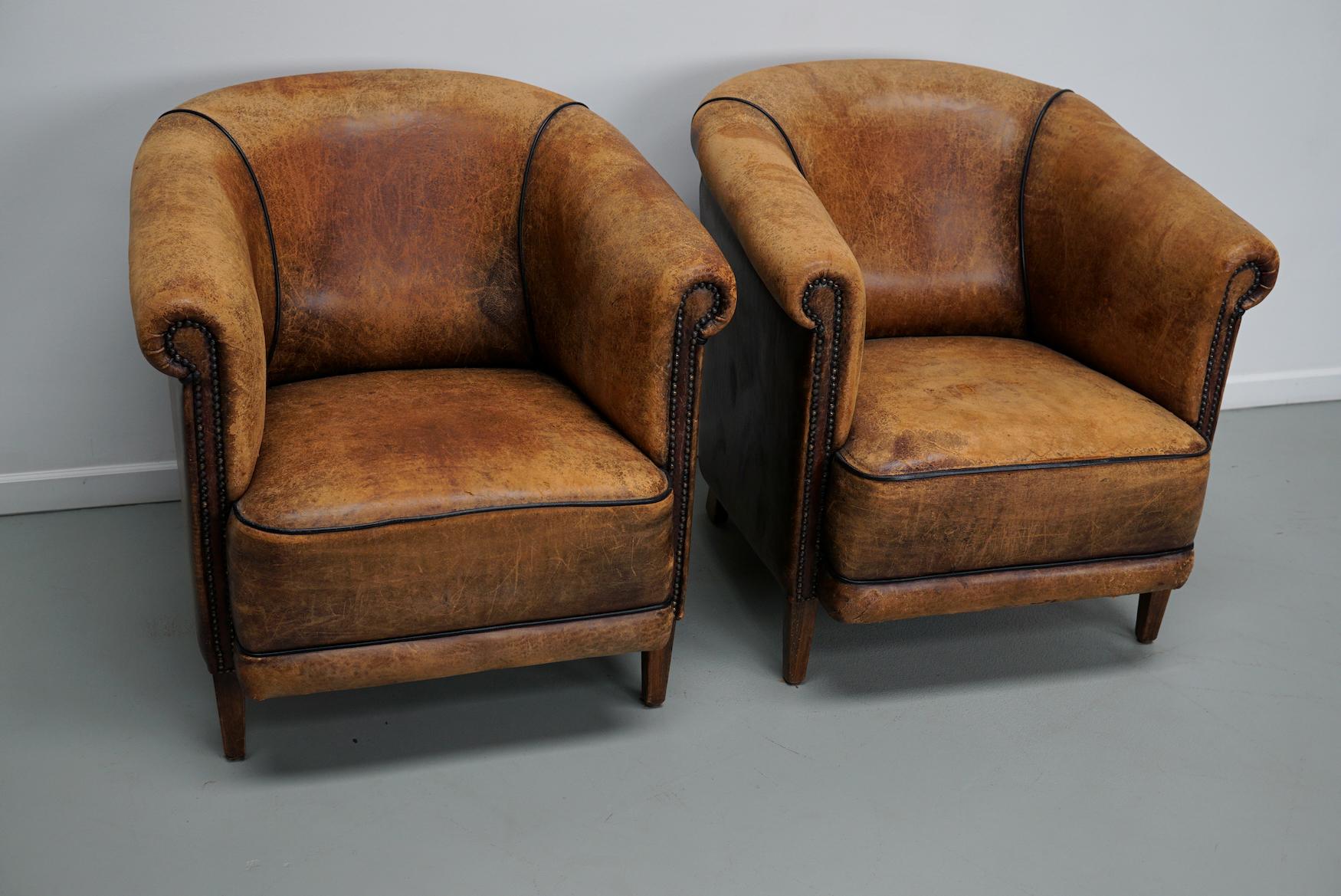 This pair of cognac-colored leather club chairs come from the Netherlands. They are upholstered with cognac-colored leather and feature metal rivets and wooden legs.