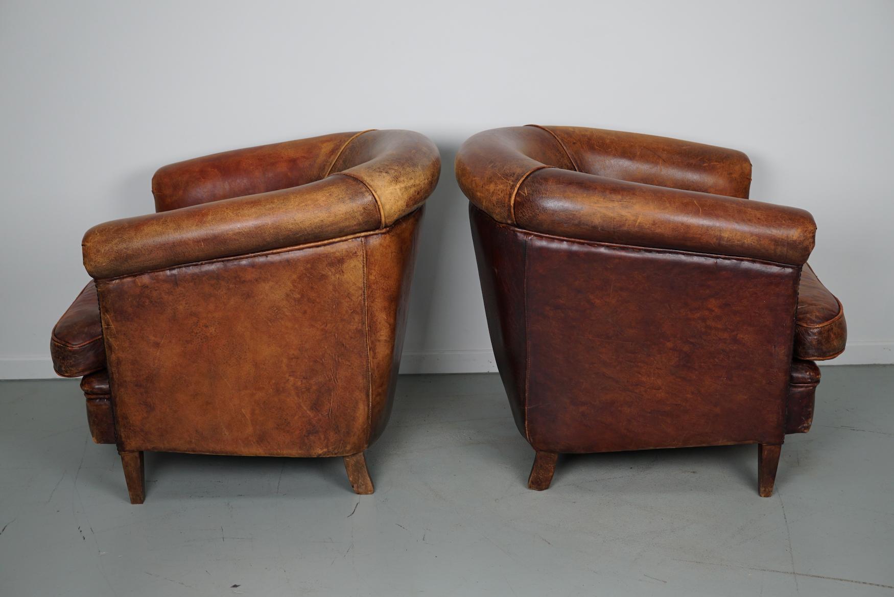 This pair of cognac-colored leather club chairs come from the Netherlands. They are upholstered with cognac-colored leather and feature metal rivets and wooden legs.