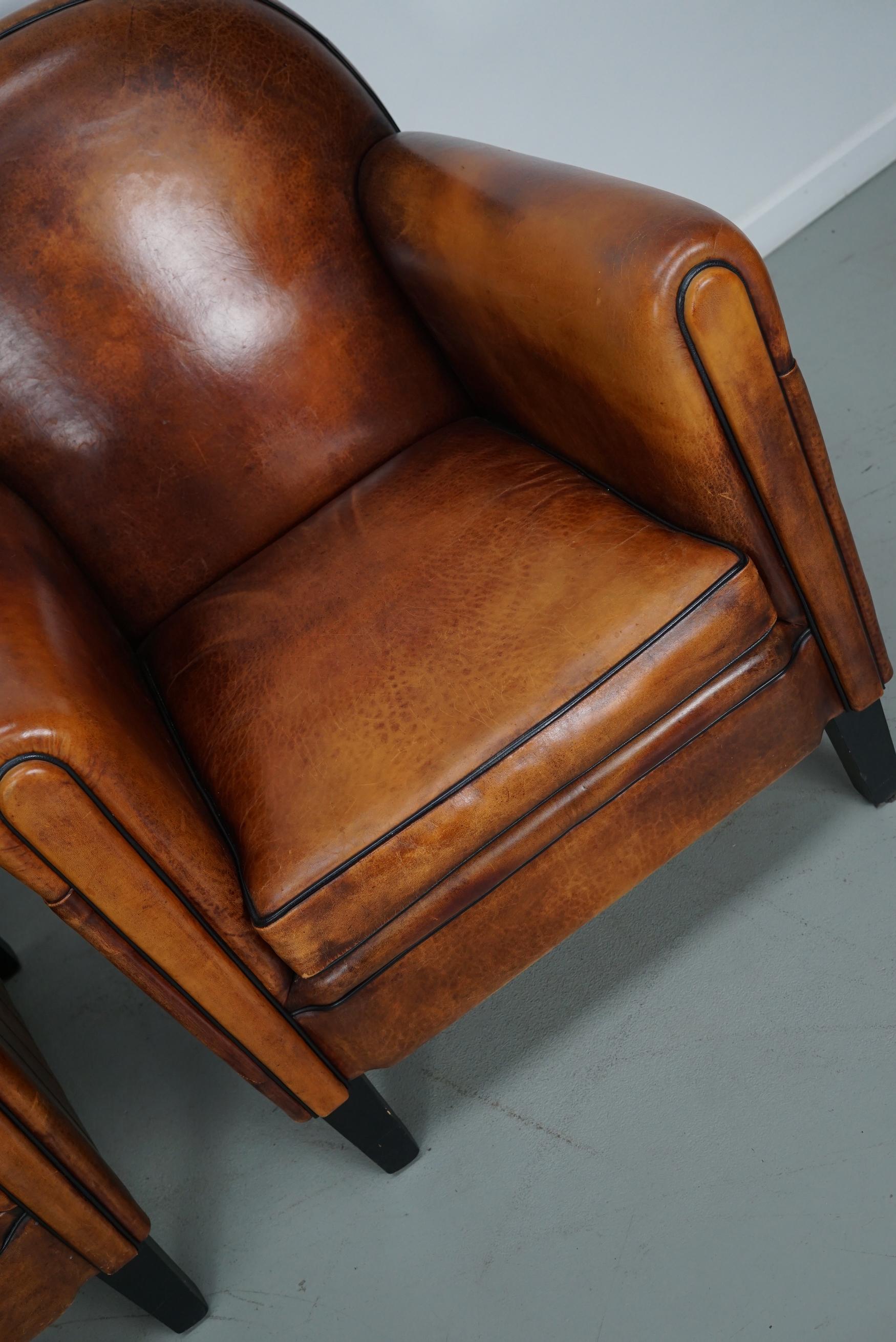 Este par de sillones club de cuero de color coñac proceden de los Países Bajos. Están tapizados en piel de color coñac y presentan remaches metálicos y patas de madera.