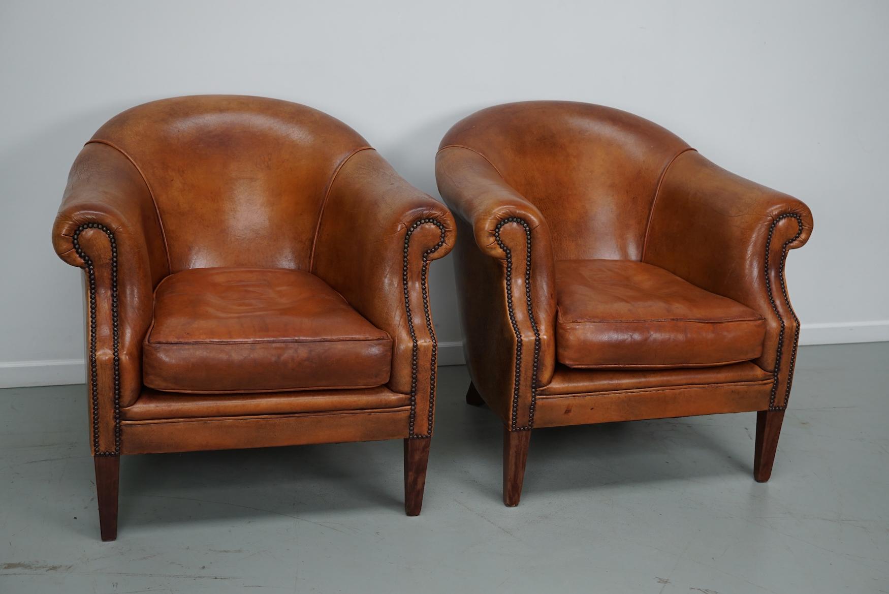 Cette paire de fauteuils club en cuir de couleur cognac provient des Pays-Bas. Ils sont recouverts de cuir de couleur cognac et présentent des rivets en métal et des pieds en bois.