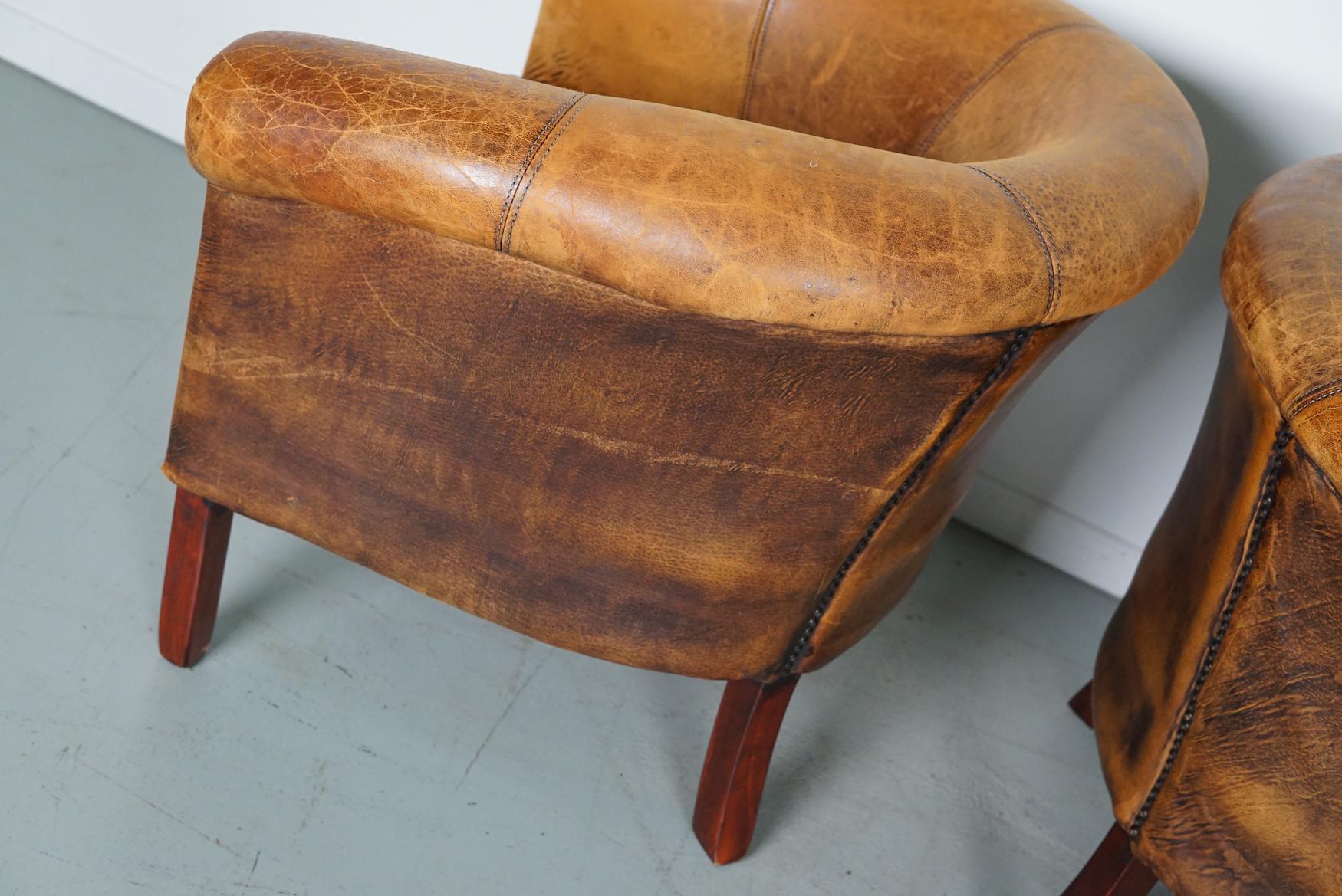 This pair of cognac-colored leather club chairs come from the Netherlands. They are upholstered with cognac-colored leather and feature metal rivets and wooden legs. The ottomans have the following measurements: D 39 x W 48 x H 35 cm.