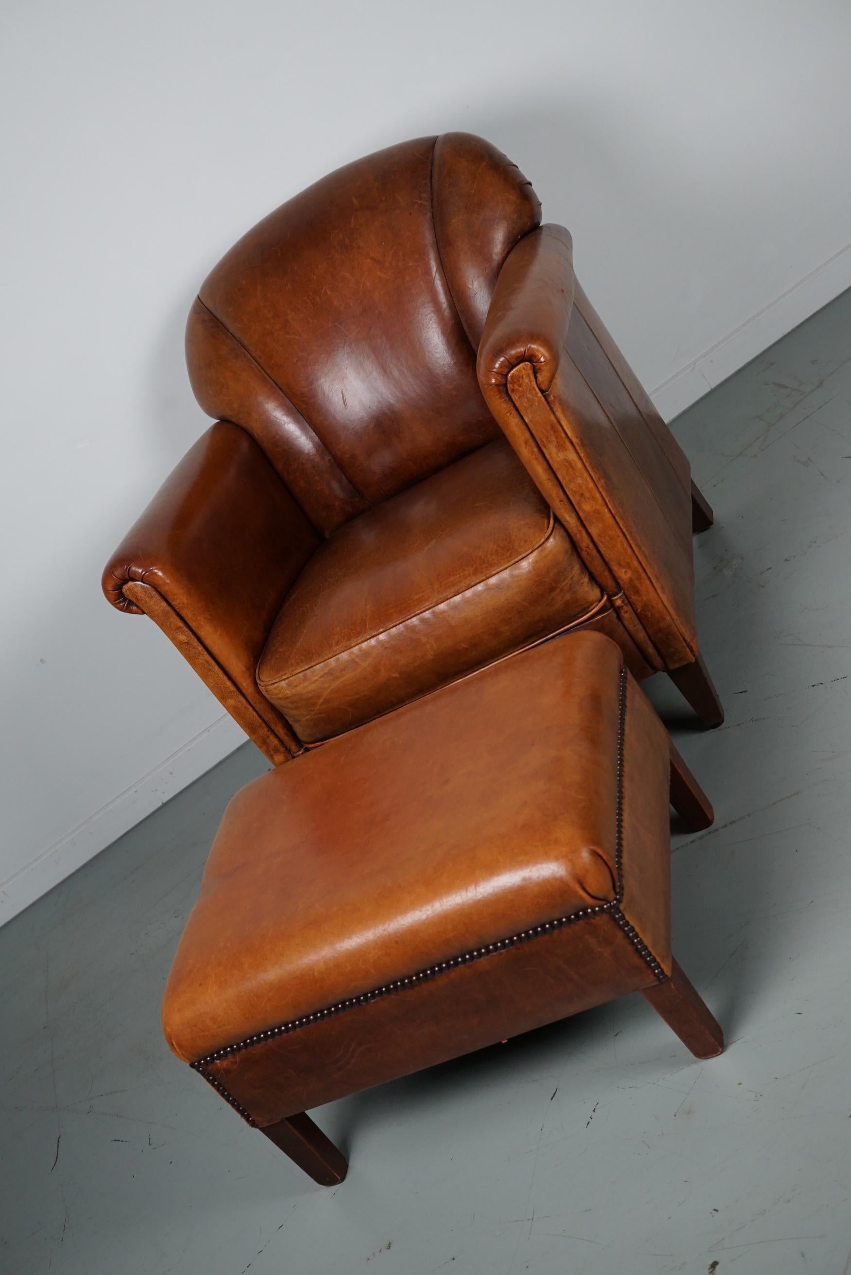 This cognac-colored leather club chair comes from the Netherlands. It is upholstered with cognac-colored leather and features metal rivets and wooden legs. The measurements of the footstool are: D 49 x W 61 x H 36 cm.