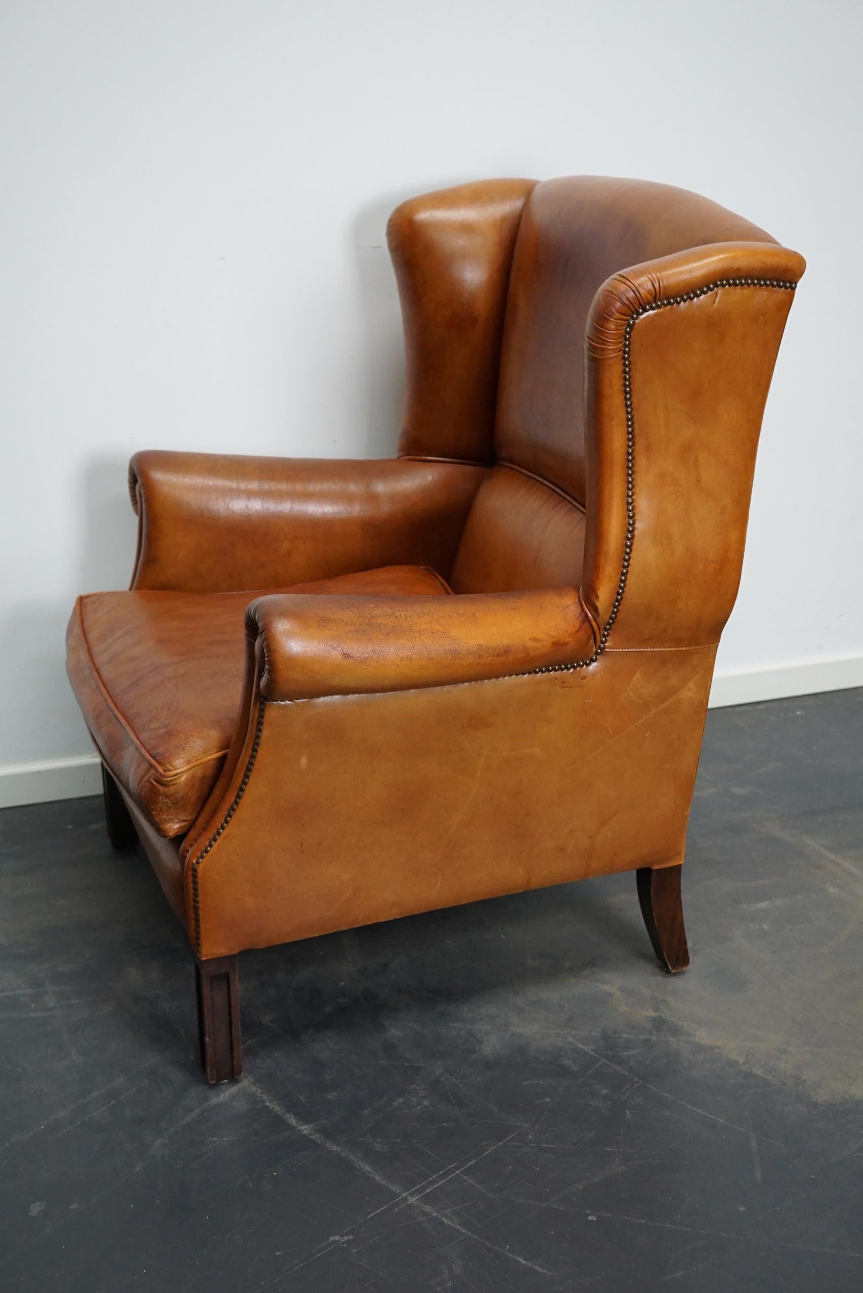 This vintage club chair is upholstered with cognac-colored leather and features metal rivets and wooden legs.