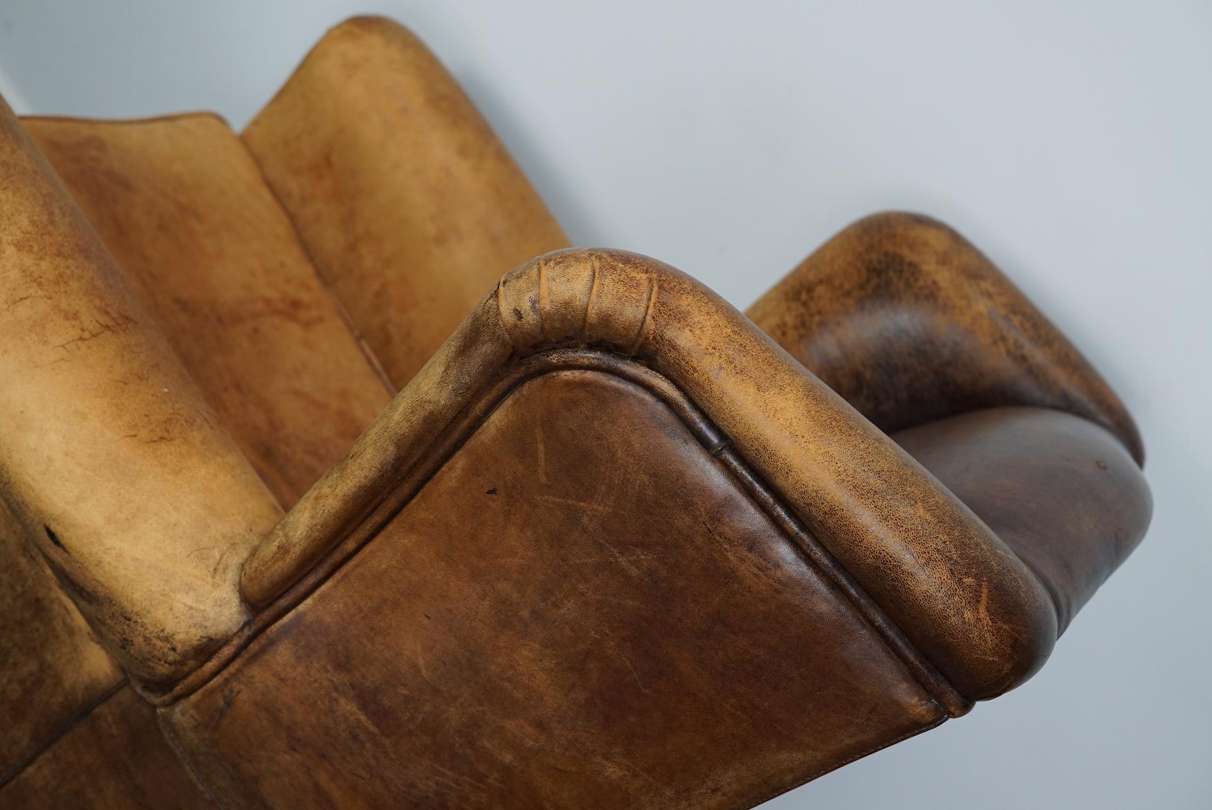 This cognac-colored leather club chair comes from the Netherlands. It is upholstered with cognac-colored leather and features metal rivets and wooden legs.