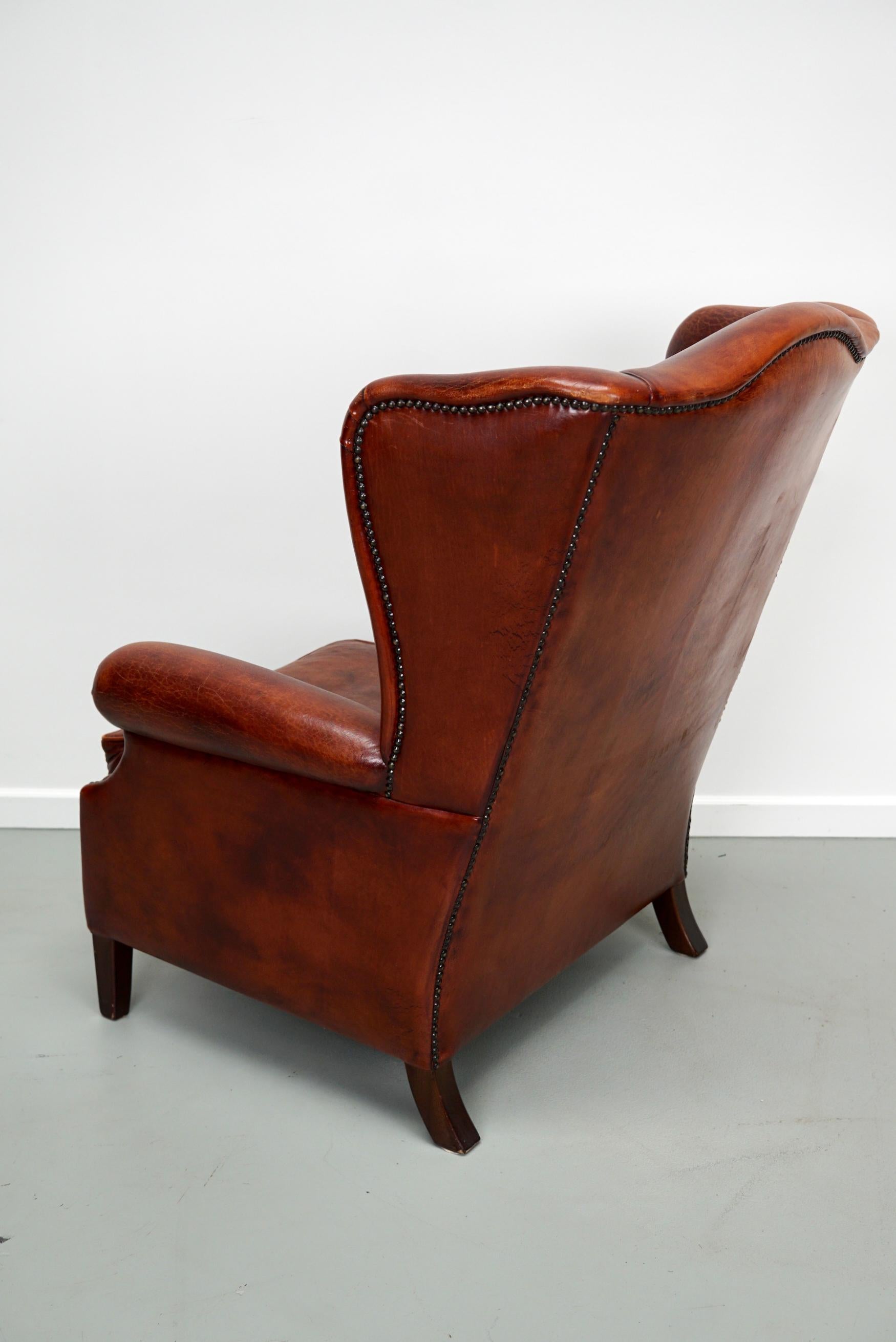 Ce fauteuil club en cuir de couleur cognac provient des Pays-Bas. Il est recouvert de cuir de couleur cognac et comporte des rivets en métal et des pieds en bois.