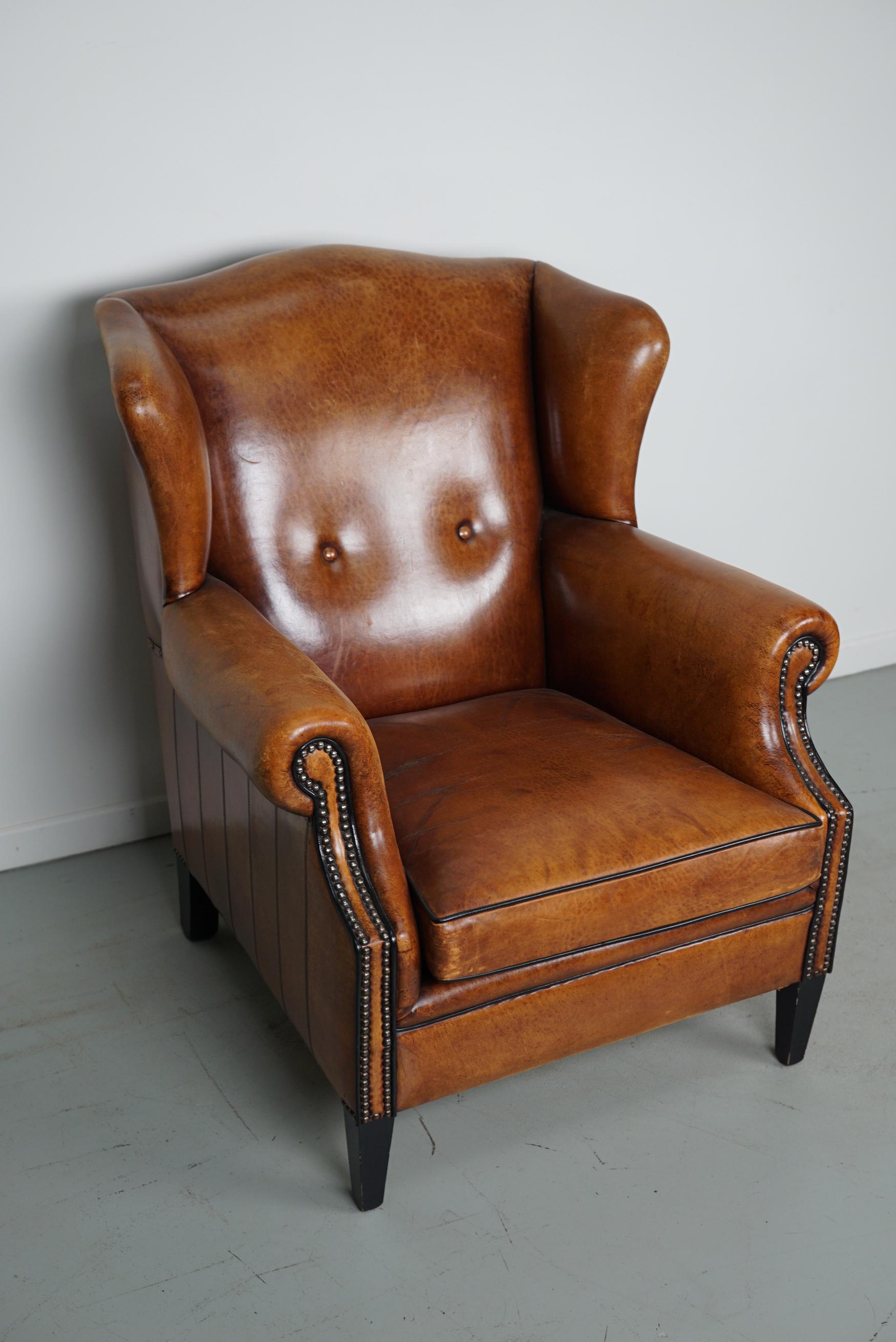 This cognac-colored leather club chair comes from the Netherlands. It is upholstered with cognac-colored leather and features black piping and wooden legs.