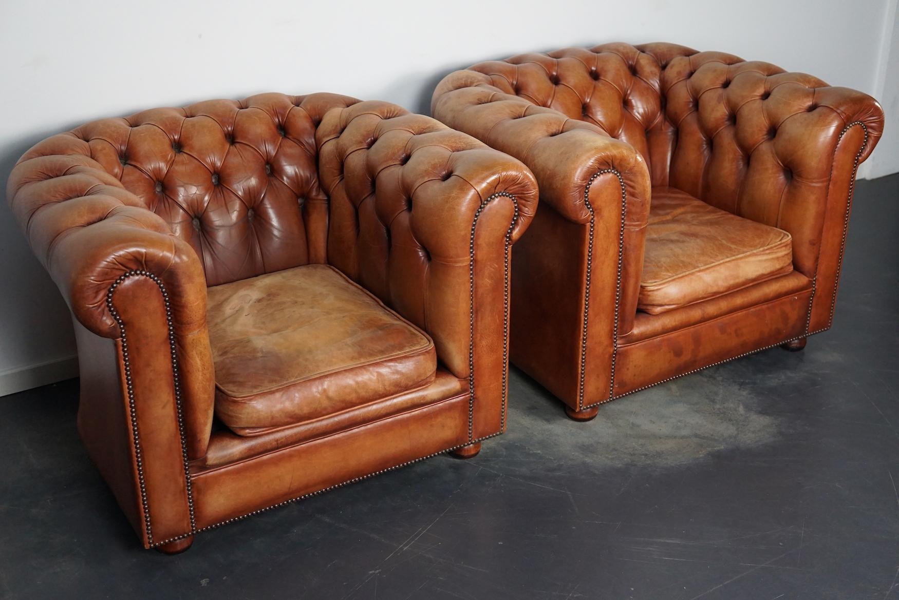 This pair of cognac-colored leather club chairs come from the Netherlands. They are upholstered with hand patinated leather and feature nails, buttoned backs and wooden legs.