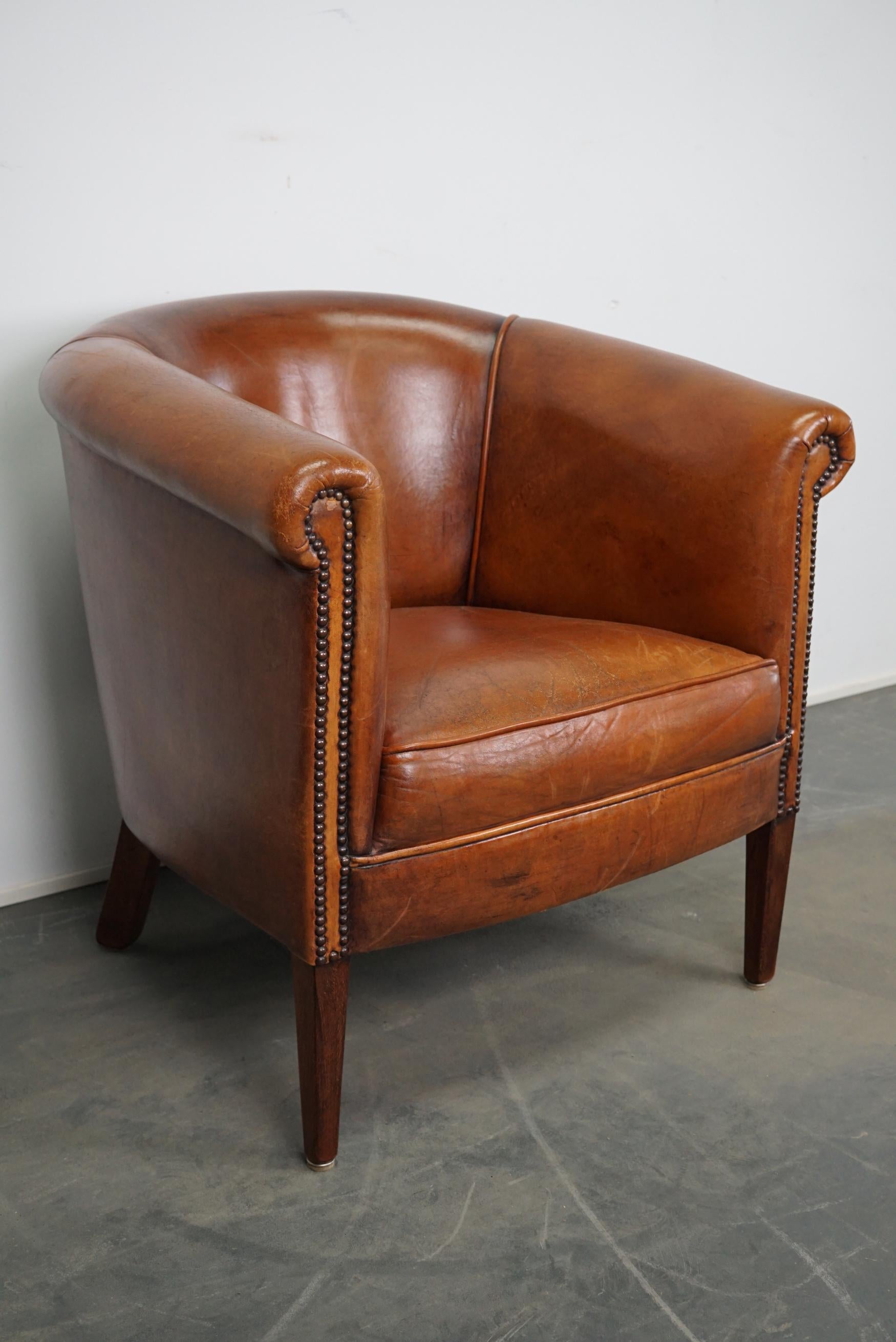 This vintage cognac-colored leather club chair comes from the Netherlands. It is upholstered with cognac-colored leather and features metal rivets and wooden legs.