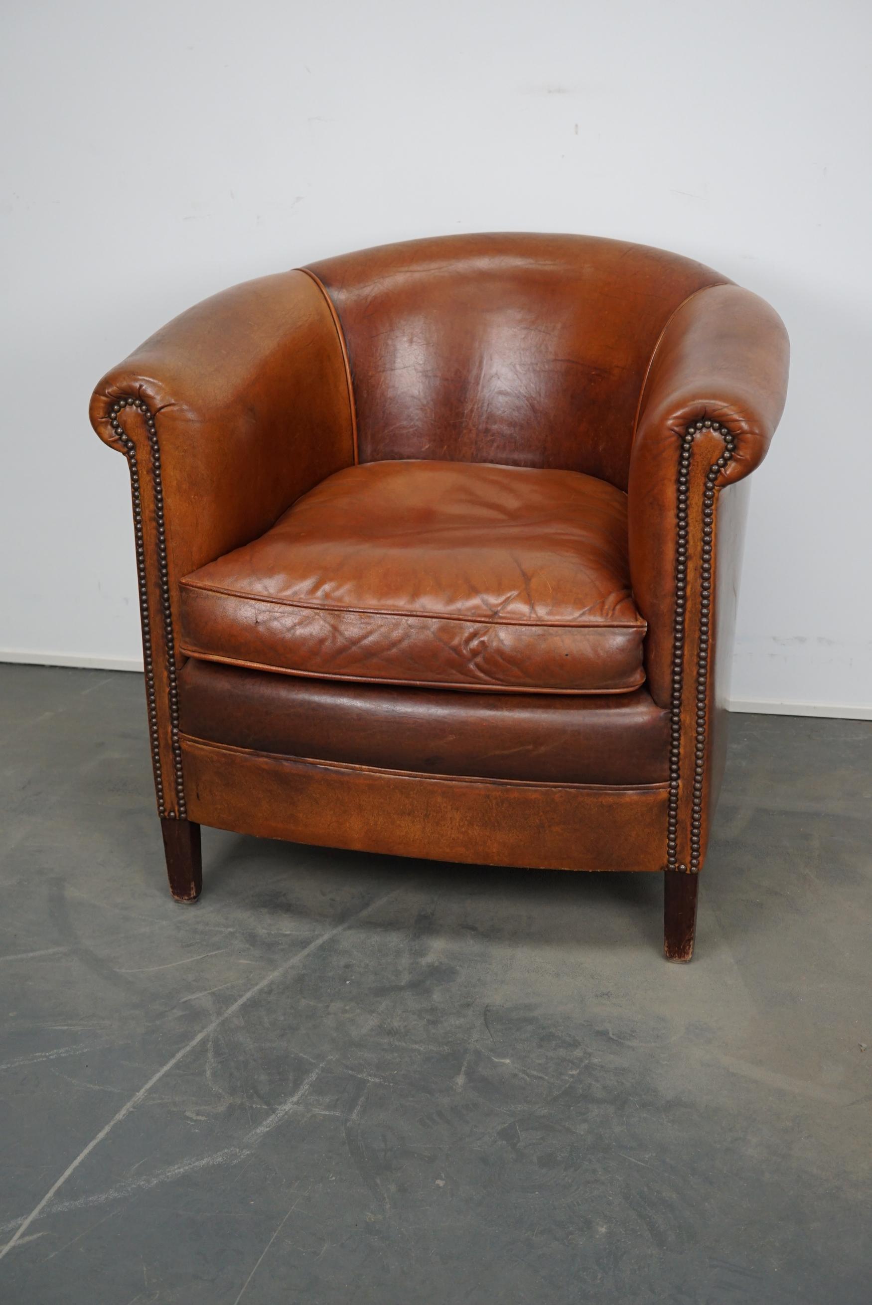 This vintage cognac-colored leather club chair comes from the Netherlands. It is upholstered with cognac-colored leather and features metal rivets and wooden legs.