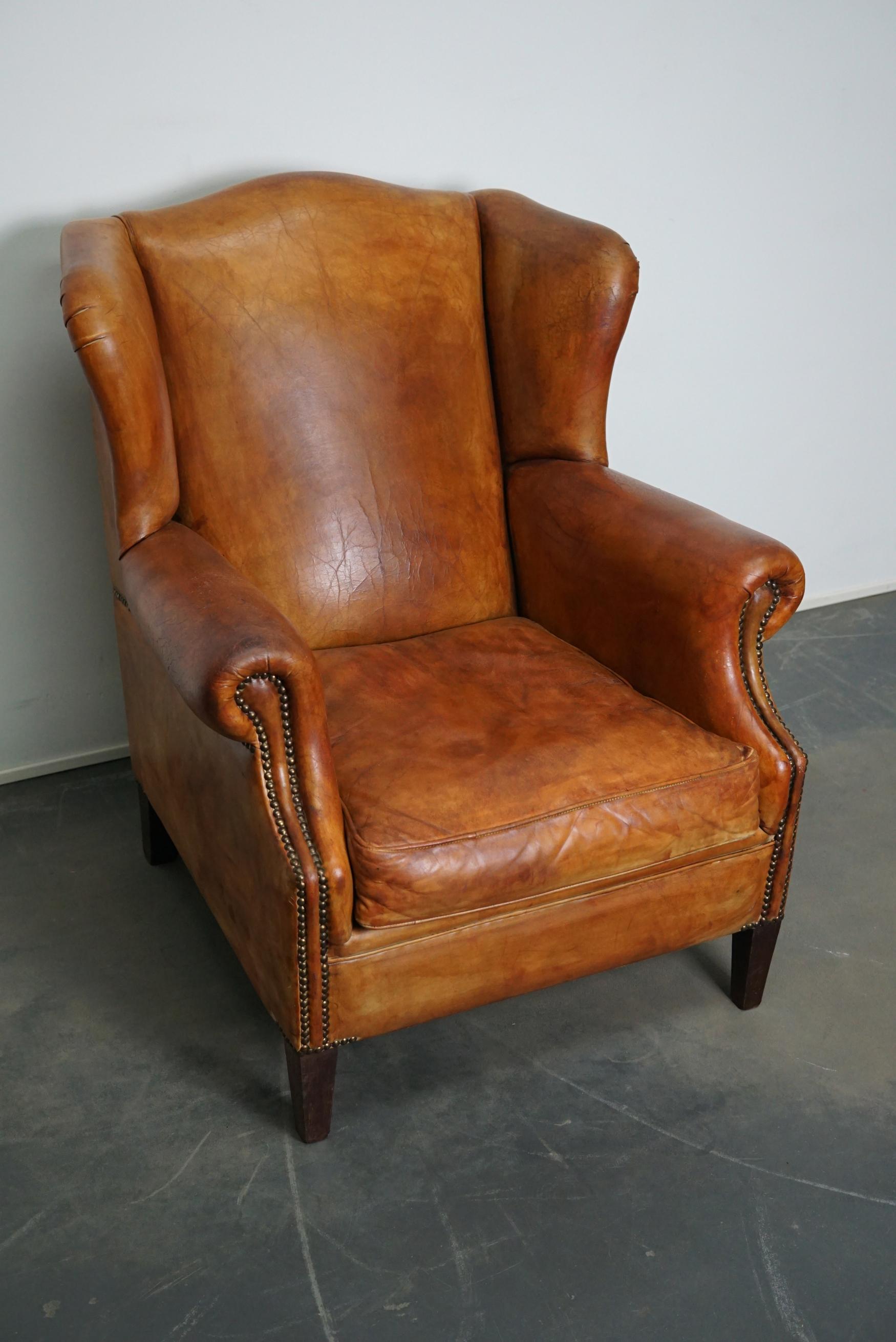 This vintage cognac-colored leather club chair comes from the Netherlands. It is upholstered with cognac-colored leather and features metal rivets and wooden legs.