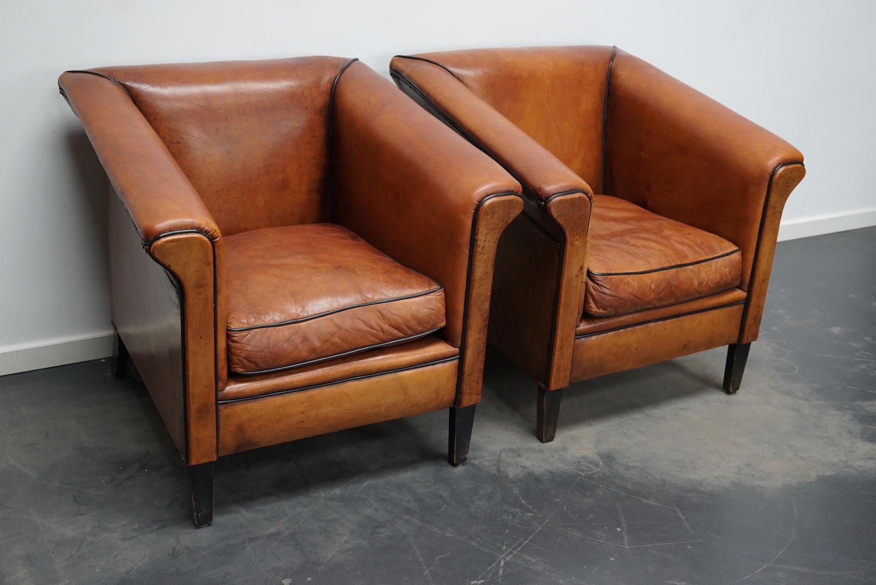 This pair of cognac-colored leather club chairs come from the Netherlands. They are upholstered with hand patinated leather and feature nails and wooden legs.