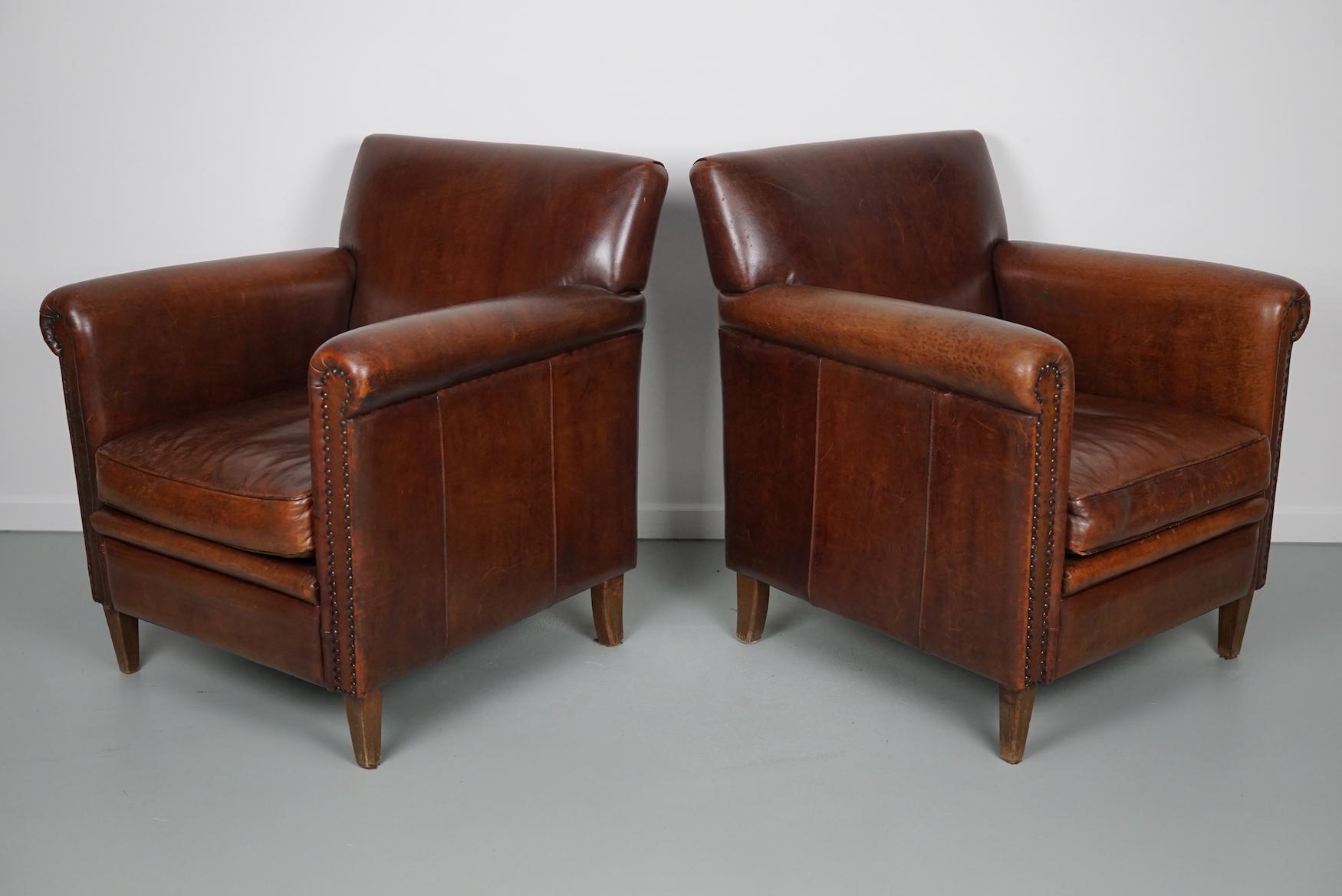 This pair of cognac/burgundy-colored leather club chairs come from the Netherlands. They are upholstered with hand patinated leather and feature nails and wooden legs.