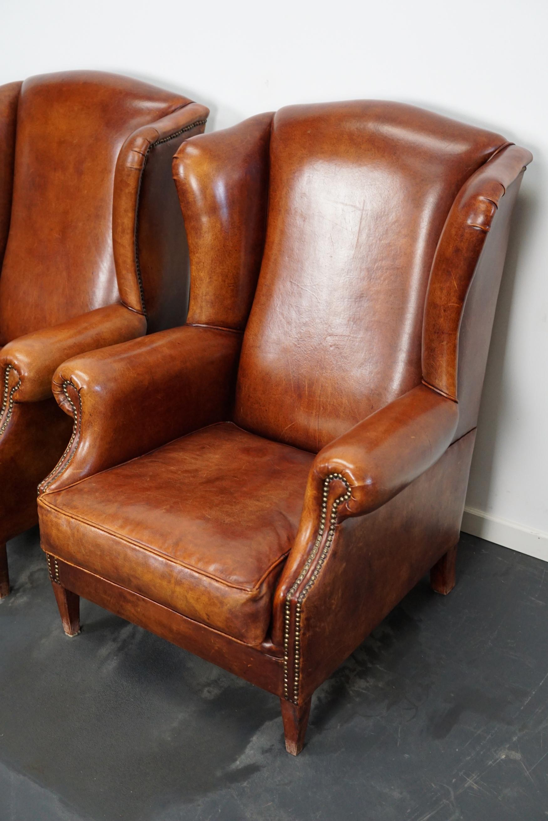 This pair of cognac-colored leather club chairs come from the Netherlands. They are upholstered with hand patinated leather and feature nails and wooden legs.