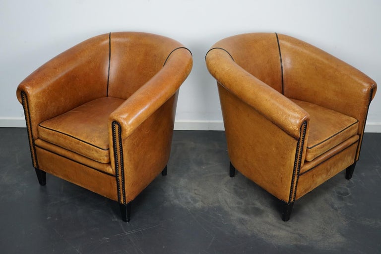 This pair of cognac/burgundy-colored leather club chairs come from the Netherlands. They are upholstered with hand patinated leather and feature black piping and wooden legs.
