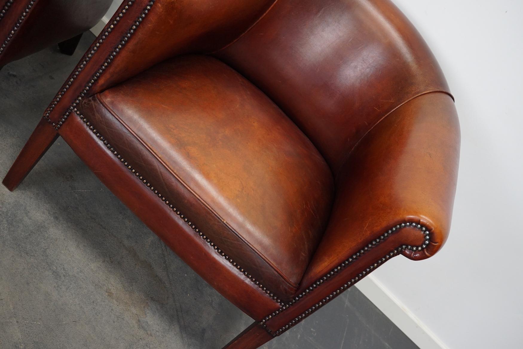 This pair of cognac/burgundy-colored leather club chairs come from the Netherlands. They are upholstered with hand patinated leather attached with nails on wooden legs.