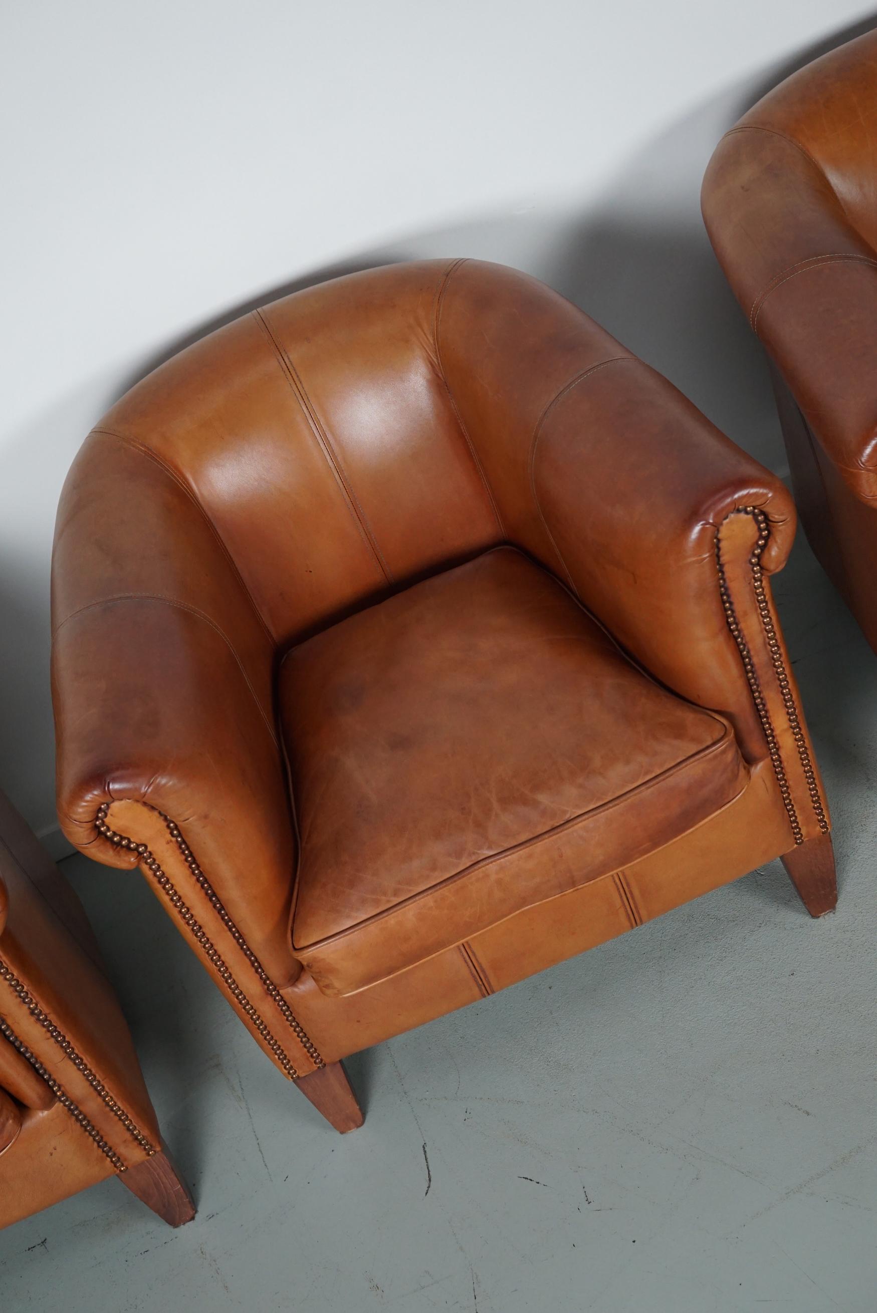This set of three cognac-colored leather club chairs come from the Netherlands. They are upholstered with cognac-colored leather and feature metal rivets and wooden legs. This set also includes two footstools which is quite uncommon.