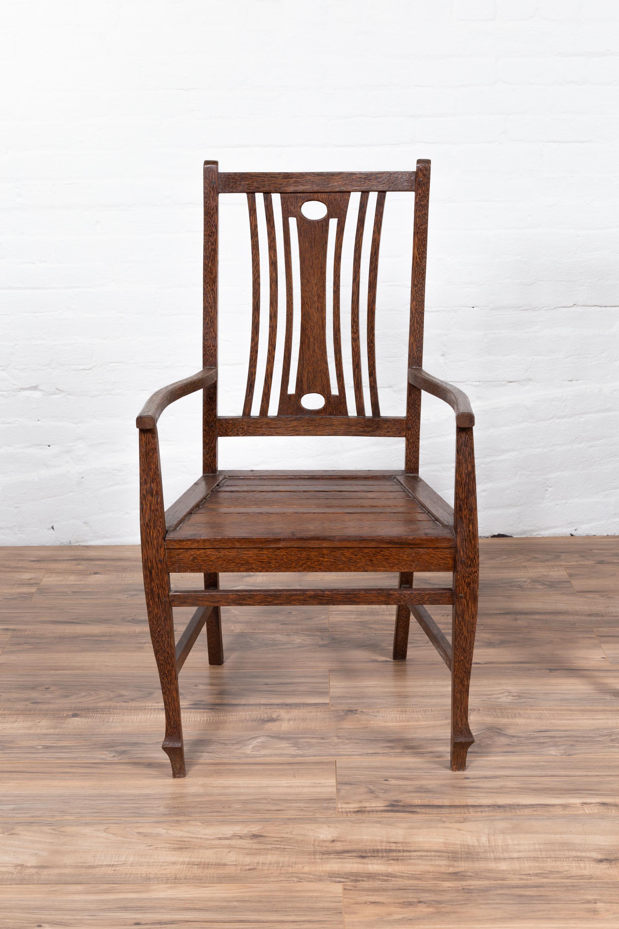 A vintage Dutch Colonial armchair from the mid-20th century, with pierced back splat and wooden slats on the seat. We currently have five chairs available, priced and sold individually. Born in Indonesia during the mid-century period, this Dutch