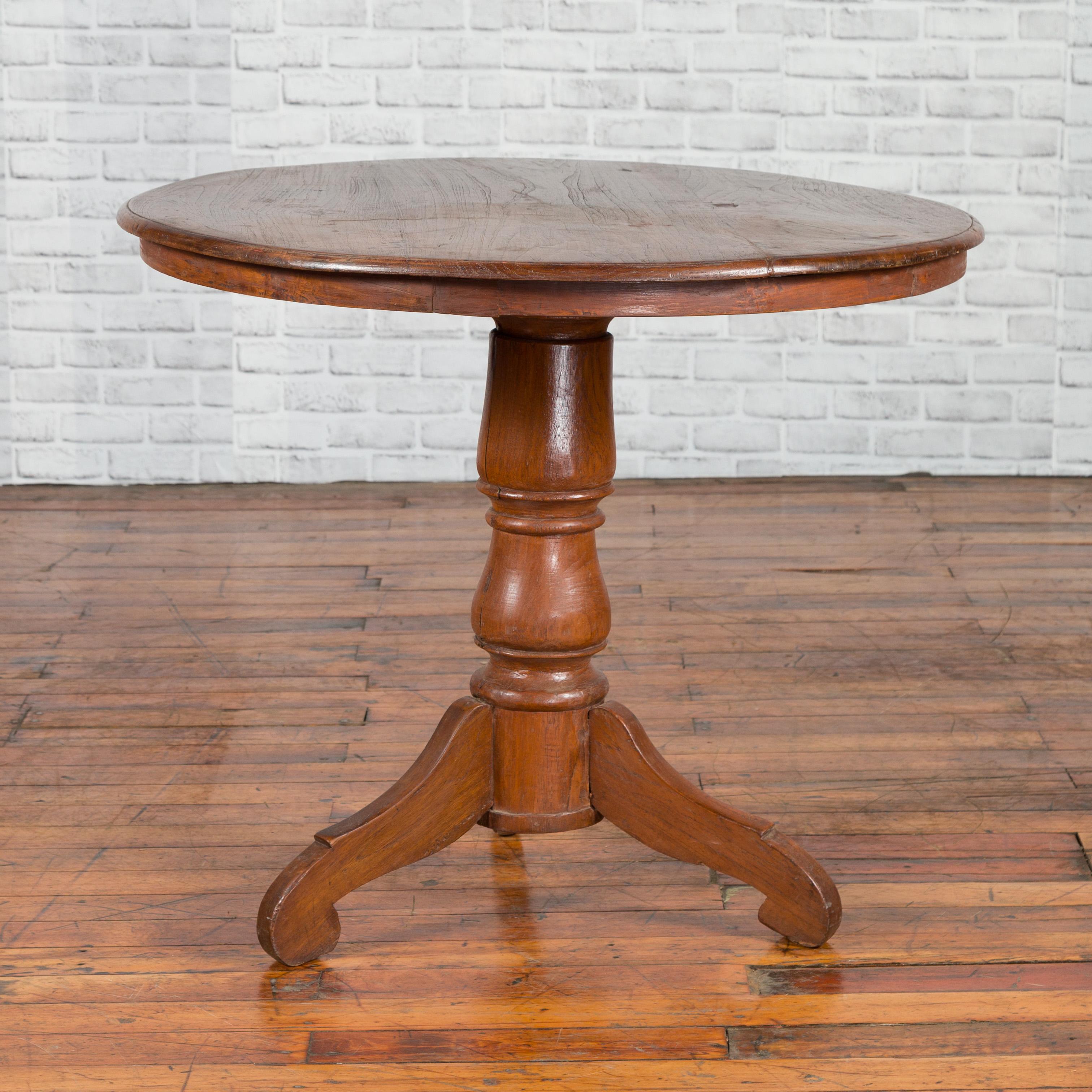 A vintage Indonesian Dutch Colonial round table from the mid-20th century, with pedestal and tripod base. Created during the Dutch Colonial period, this side table features a circular top sitting above a turned pedestal resting on three scrolling