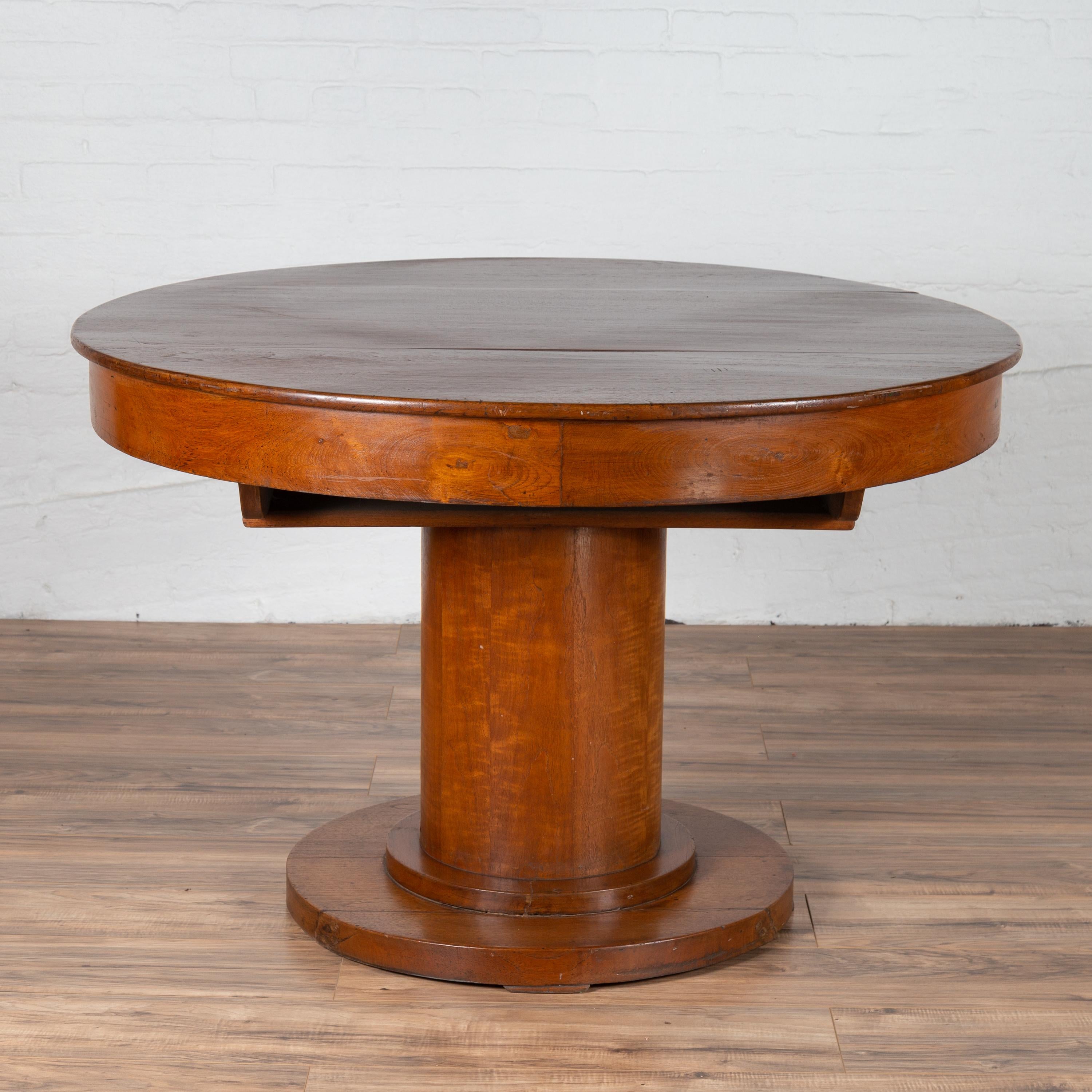 A vintage Dutch Colonial Javanese teak pedestal dining table from the mid-20th century, with circular top and cylindrical base. Born on the Island of Java during the midcentury period, this elegant pedestal table features a round planked top,