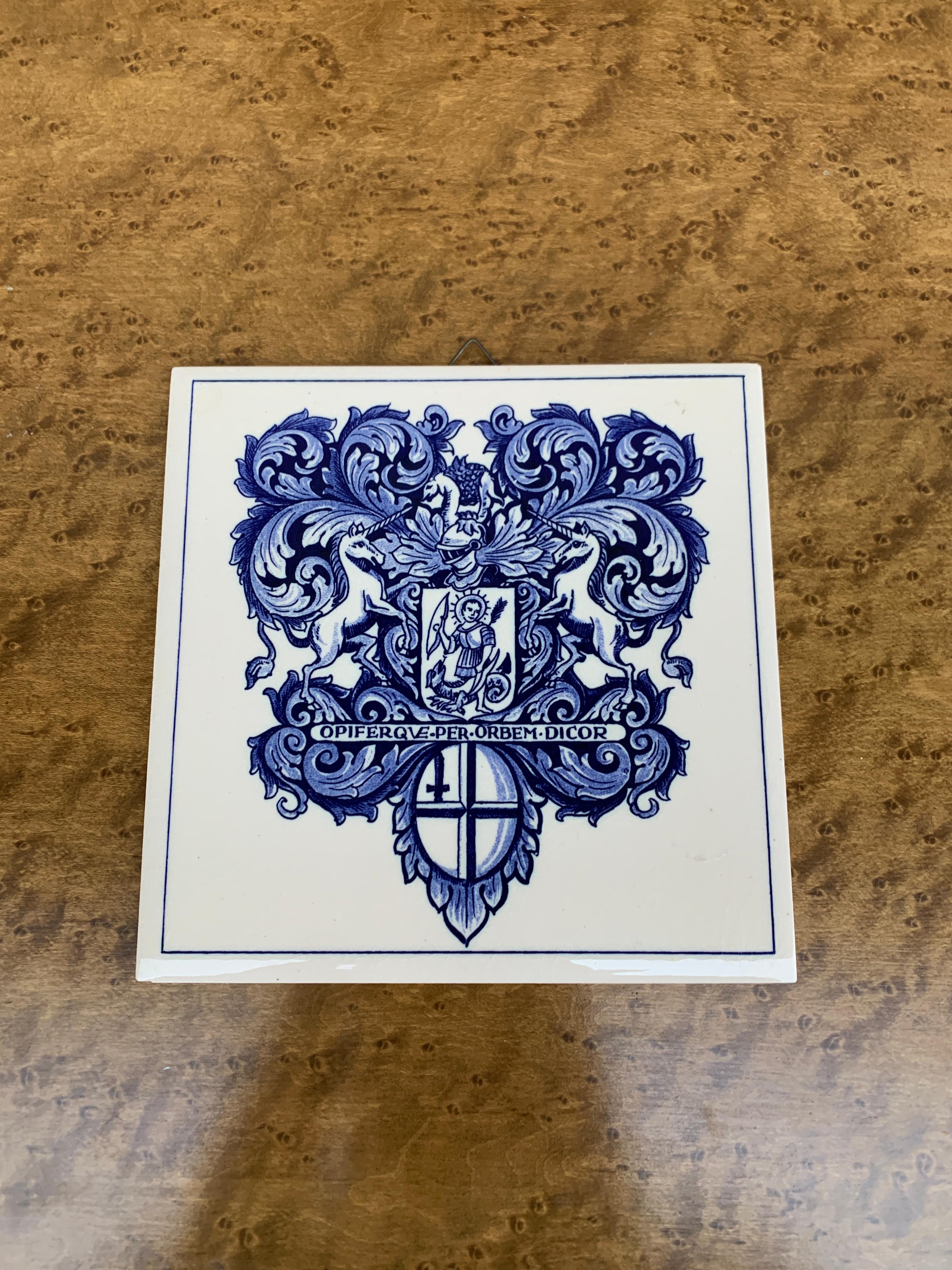 Una bellissima piastrella in ceramica dipinta a mano in bianco e blu in stile Delft o Provincia Francese, con un'armatura e un elmo di cavaliere stilizzati e uno scudo con due unicorni che si fronteggiano. All'interno del centro potrebbe esserci una