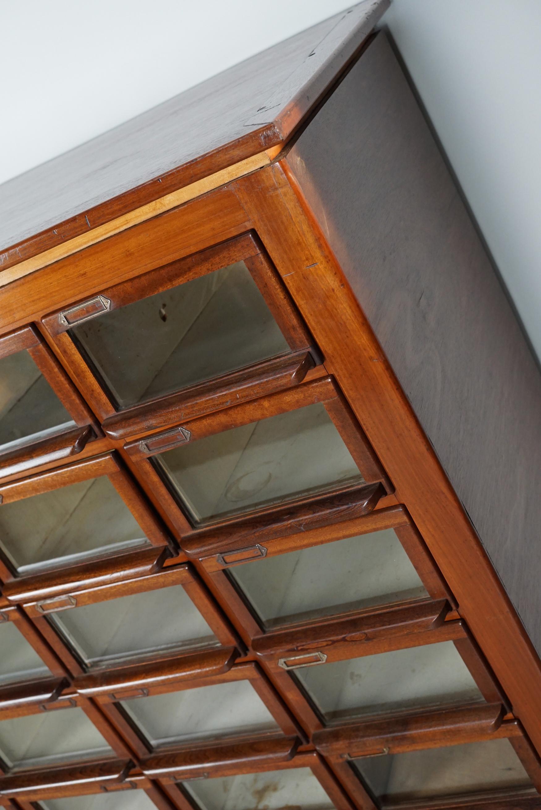 This haberdashery cabinet was produced during the 1930s in the Netherlands. This piece features 24 paper covered drawers some with glass fronts, solid handles and name card holders. It was originally used in a shop for lingerie in Amsterdam. The