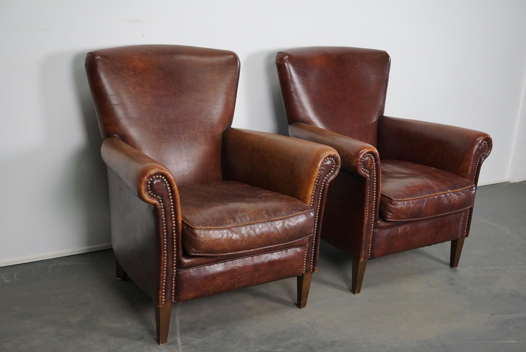 This pair of leather club chairs come from the Netherlands. They are upholstered with Bordeaux / cognac-colored leather and feature metal rivets and wooden legs. They are very comfortable.