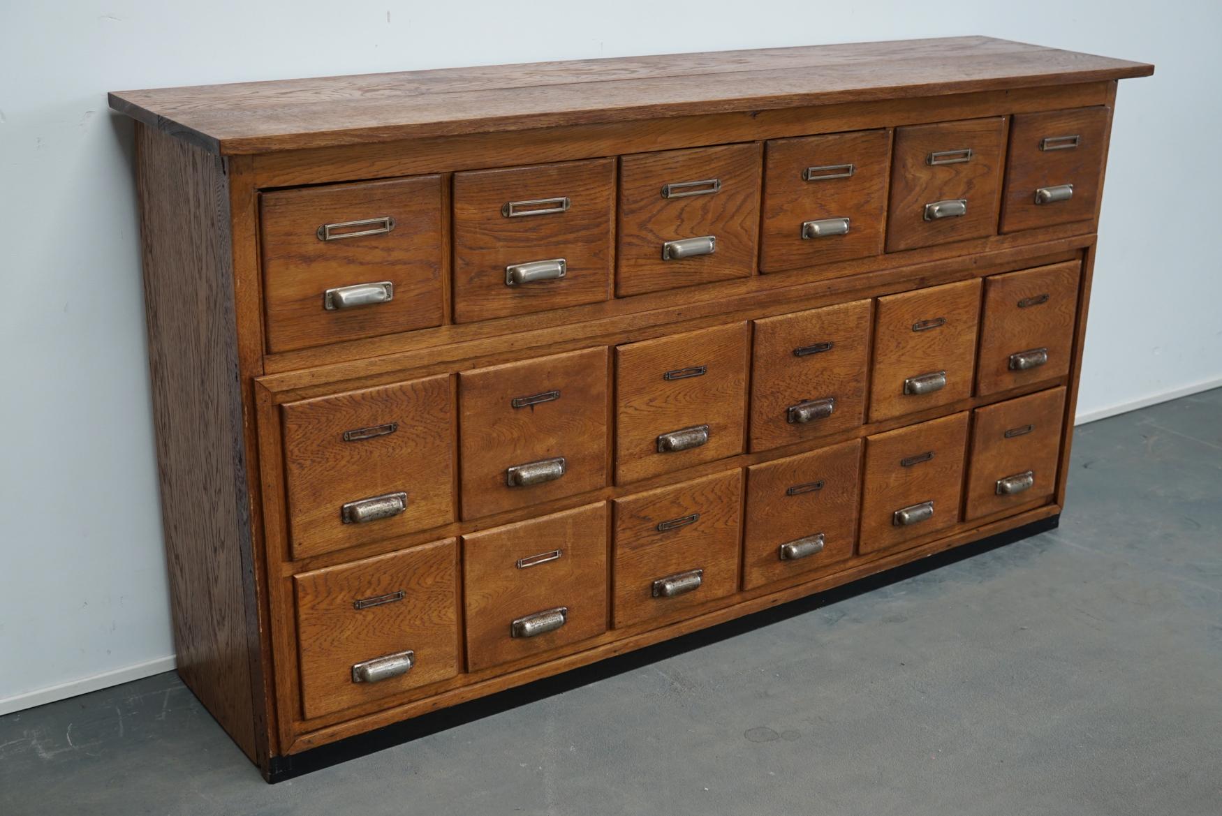 This apothecary cabinet was produced during the 1940s in the Netherlands. This piece features 18 drawers with nice metal cup handles and name card holders. It was originally used in a bakery to store the cookies. It still has most of the removable