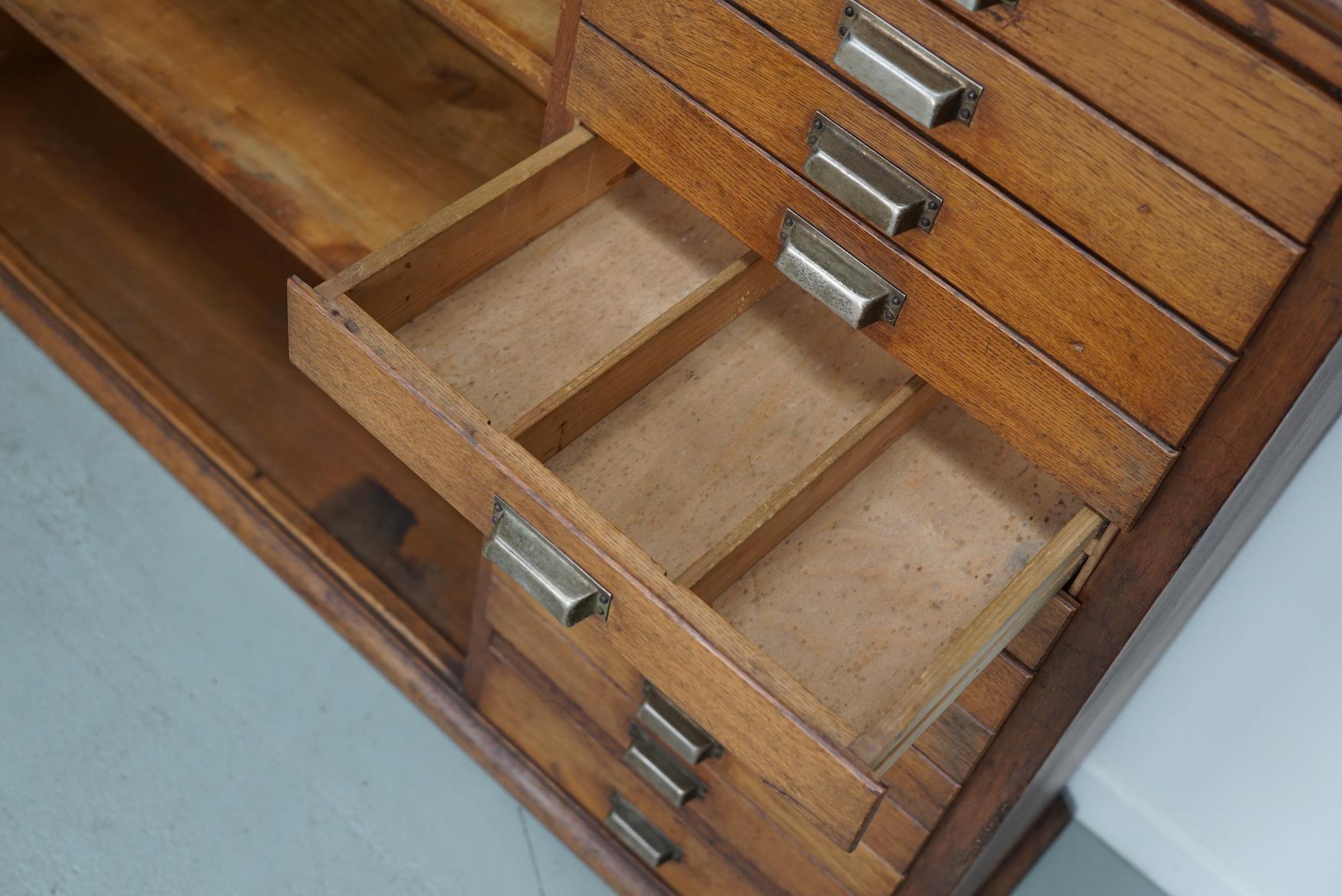 This apothecary / shop cabinet was produced during the 1950s in the Netherlands and used in a cigar shop in Den Bosch. This piece features 26 drawers with metal hardware. The interior dimensions of the drawers are: DWH 25 x 31 x 5 cm and DWH 22 x 32