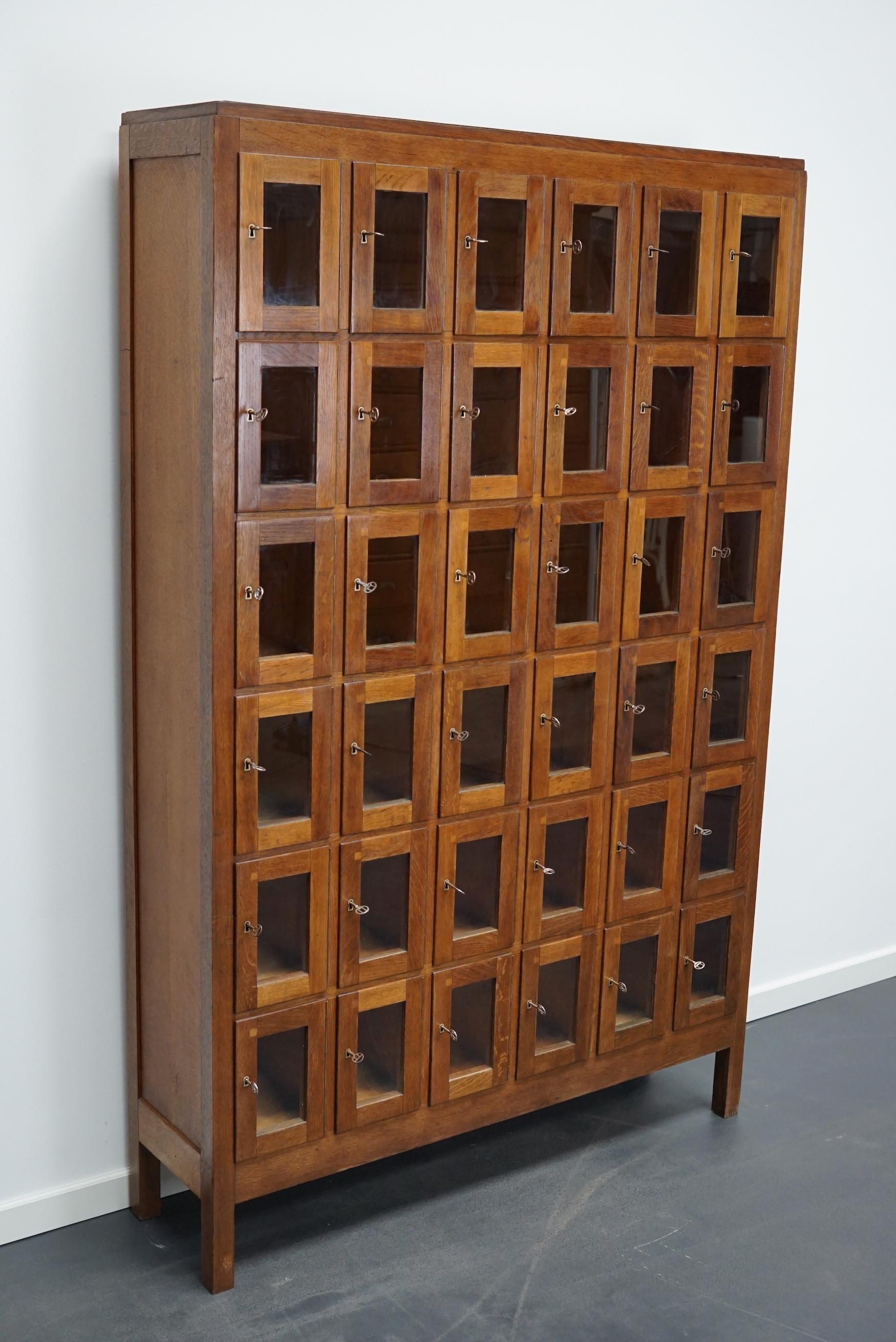 This vintage Dutch oak locker with glass doors was made around the 1930s in the Netherlands. It was used on an army base to store the headphones for the tank drivers and pilots during WW2. Every door has its own individual key. The interior